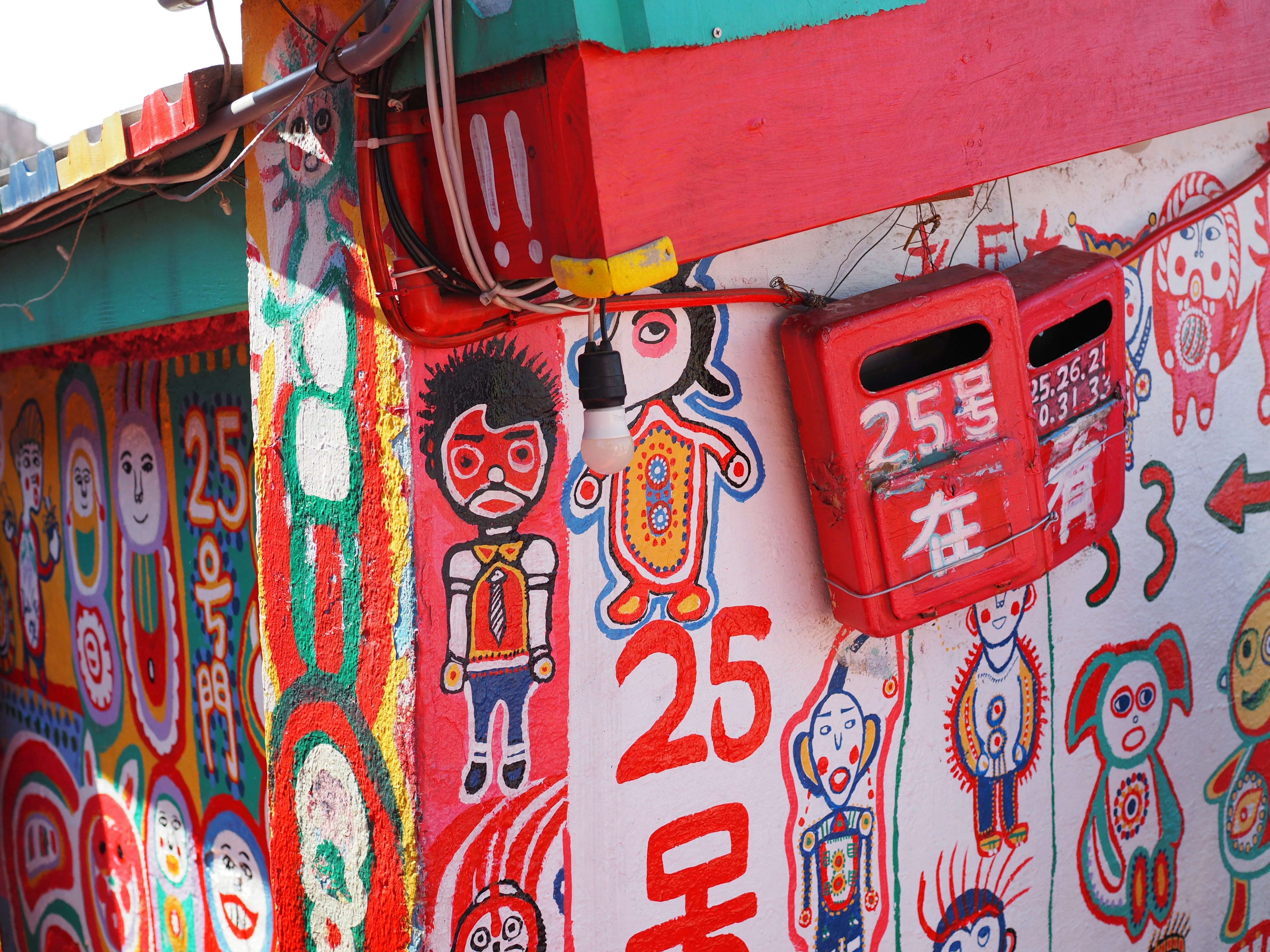 Murales coloridos en un edificio con un buzón rojo que muestra el número 25