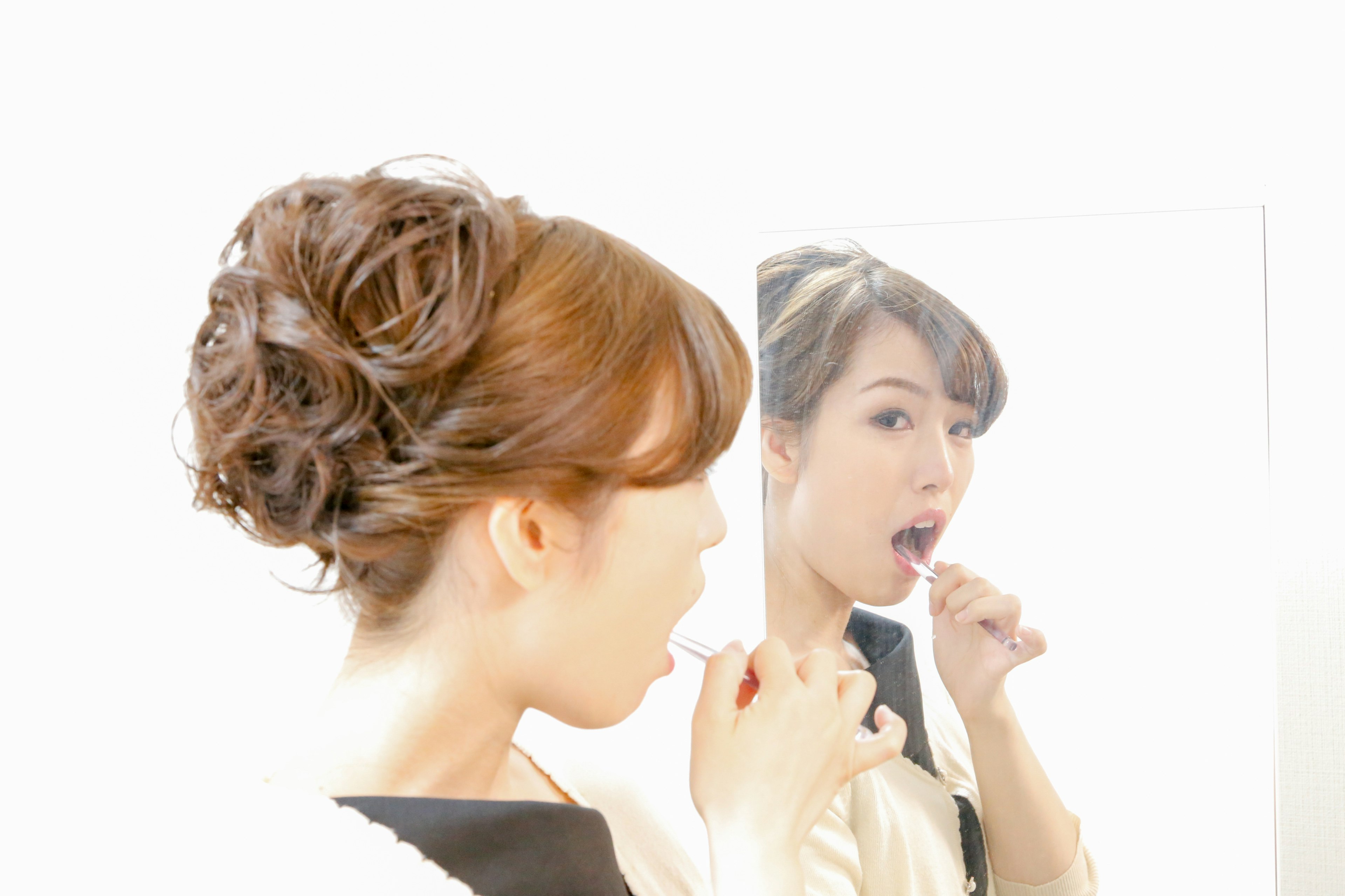 Side profile of a woman brushing her teeth in front of a mirror with a soft updo hairstyle