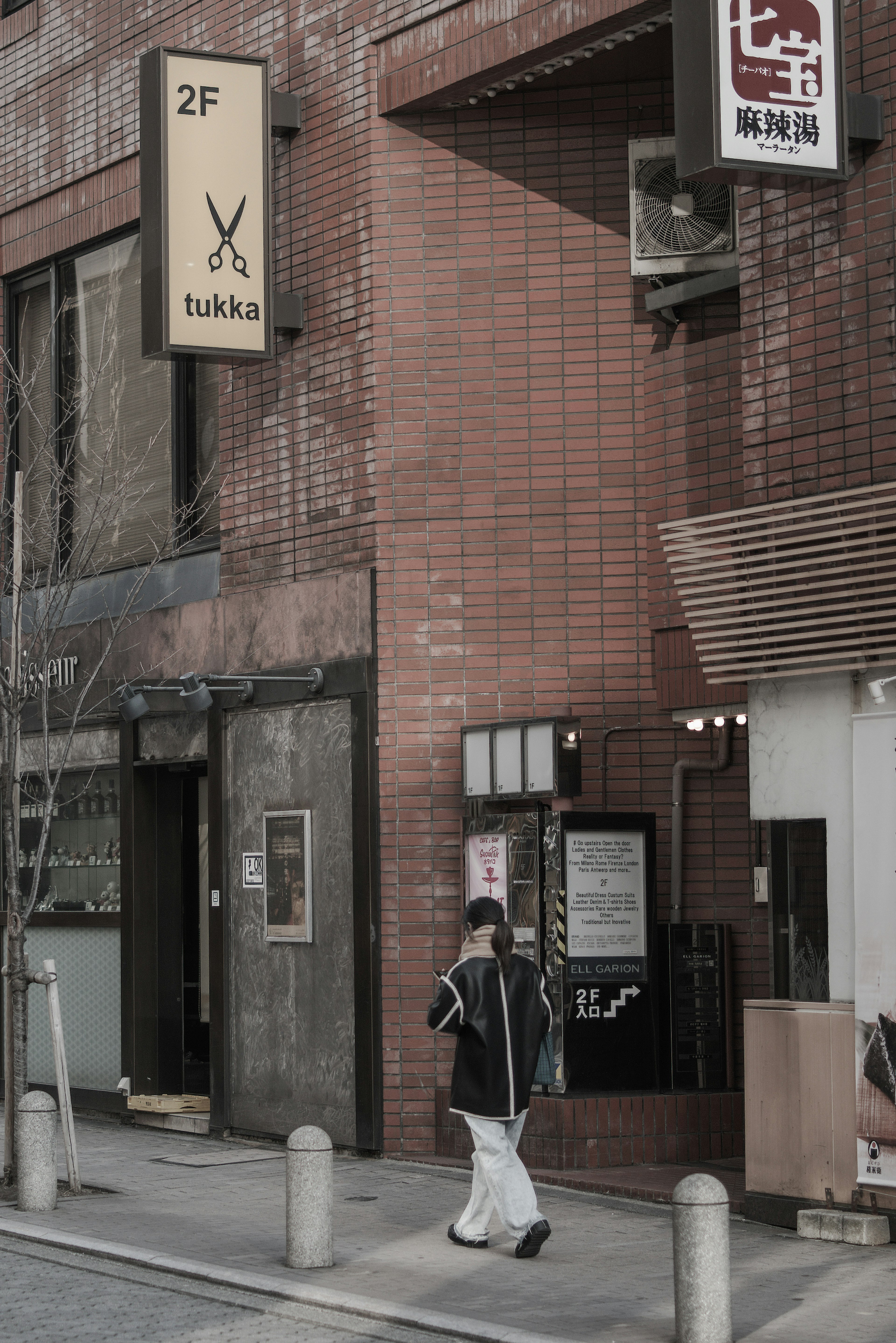 A person walking in front of a red brick building with a second-floor sign