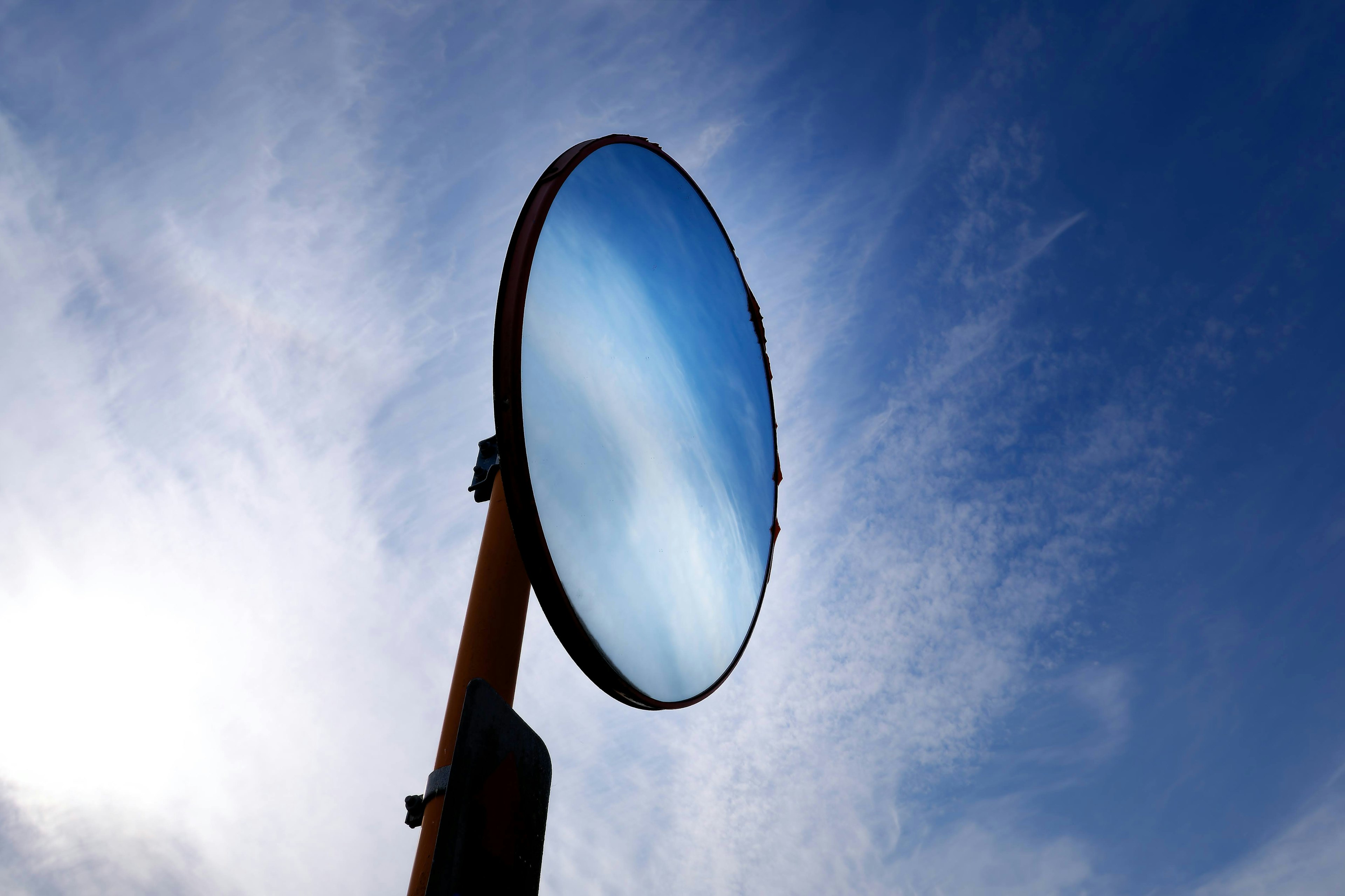 Large circular mirror reflecting blue sky mounted on a pole