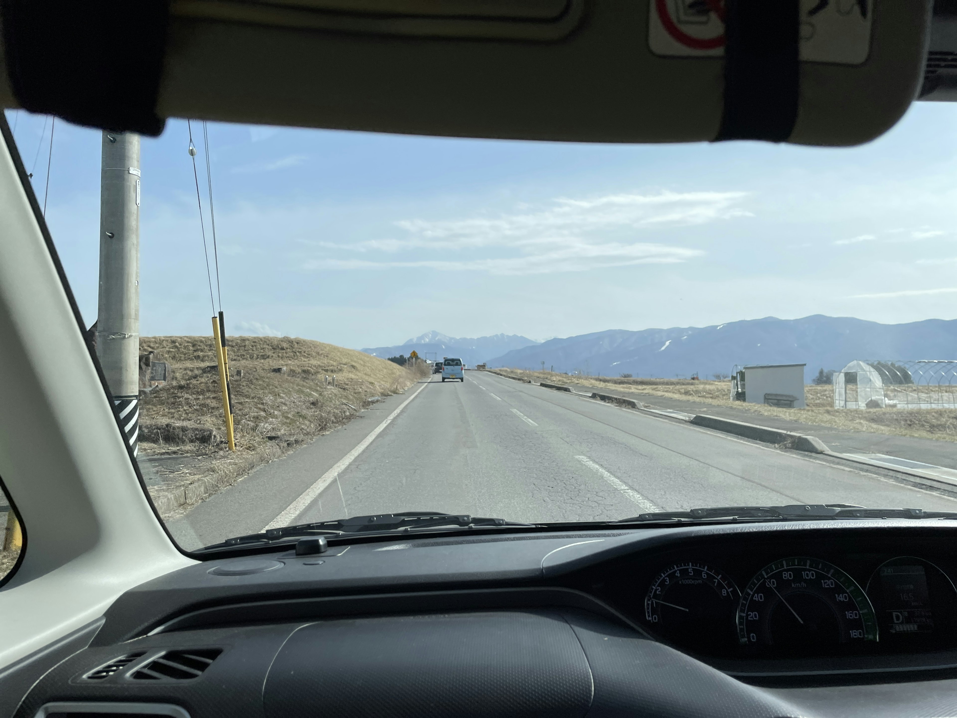 View from the driver's seat of a car on a road with mountains in the distance