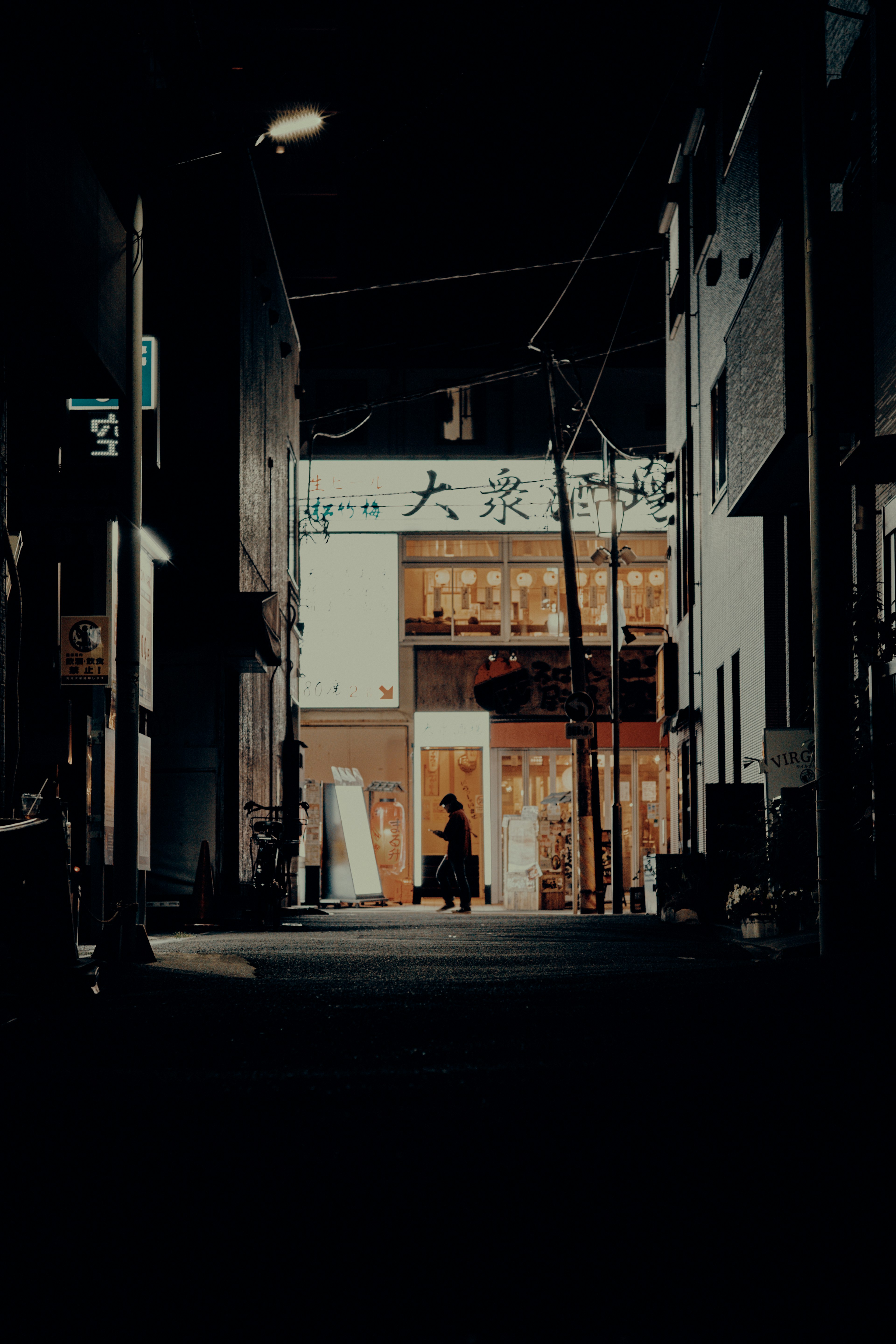 夜の街並みの小道に立つ人物と明るい店の看板