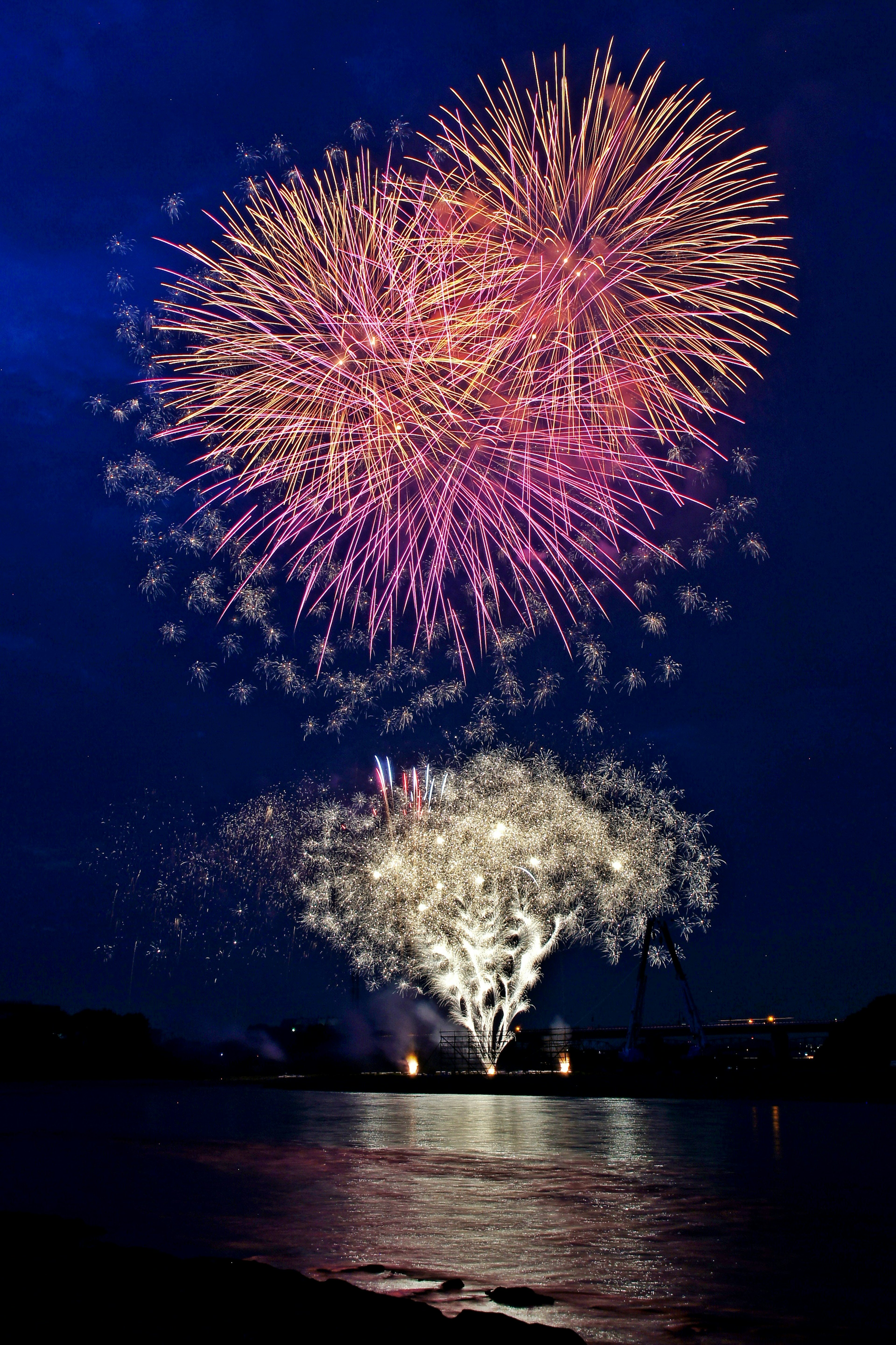 Spettacolo di fuochi d'artificio colorati che illuminano il cielo notturno riflettendosi sull'acqua