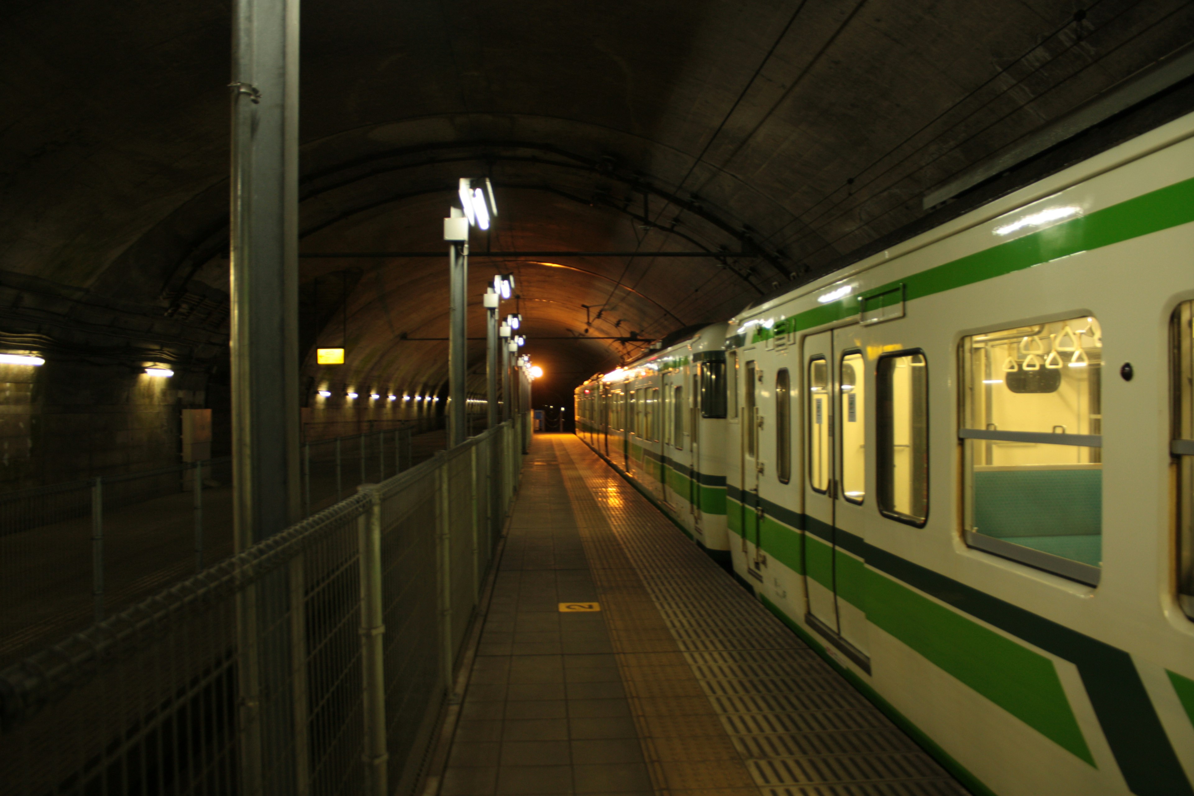 A dark subway station with a green-striped train parked in the tunnel