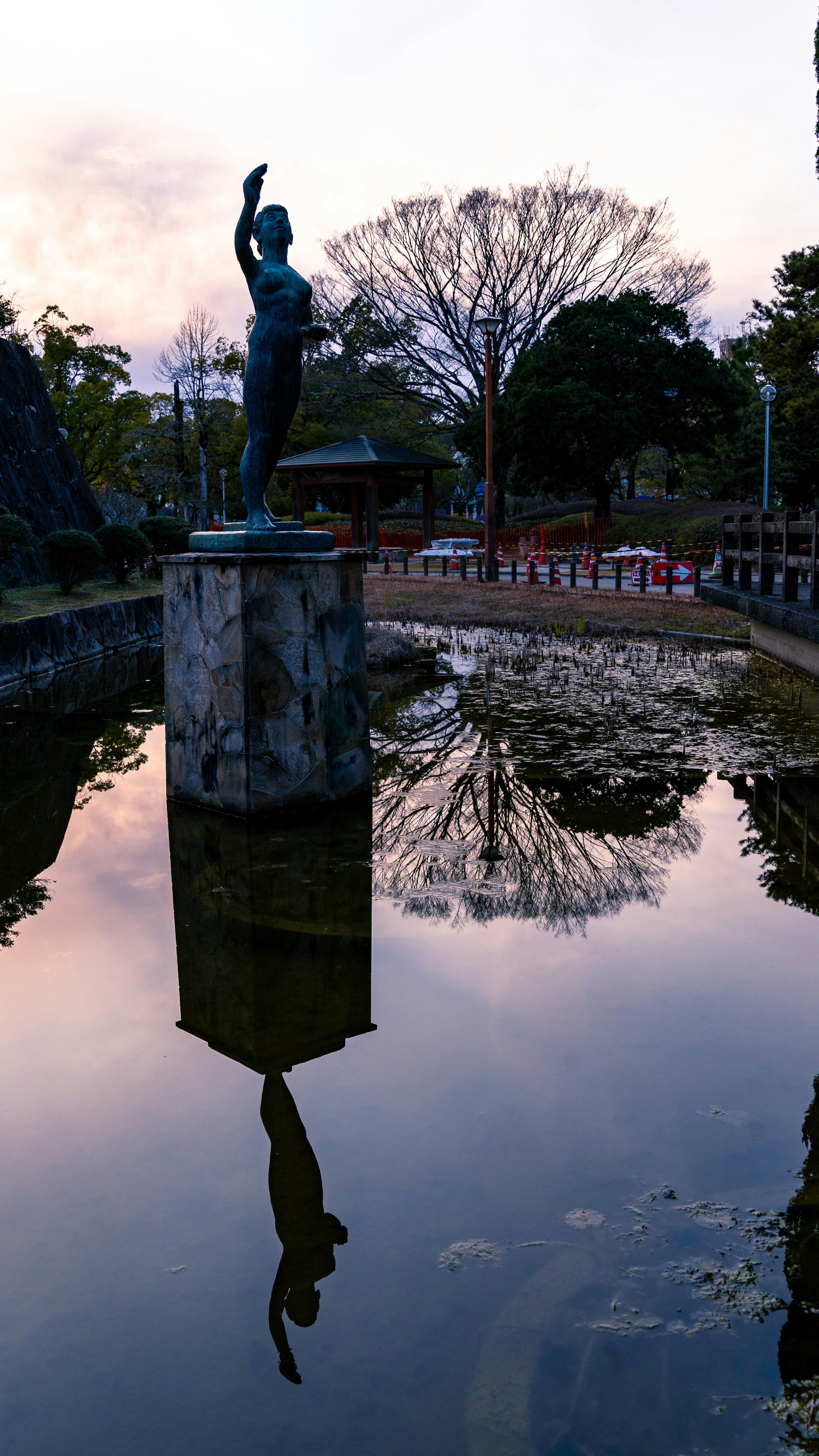 Statue auf einem Sockel neben einem ruhigen Teich mit Reflexion