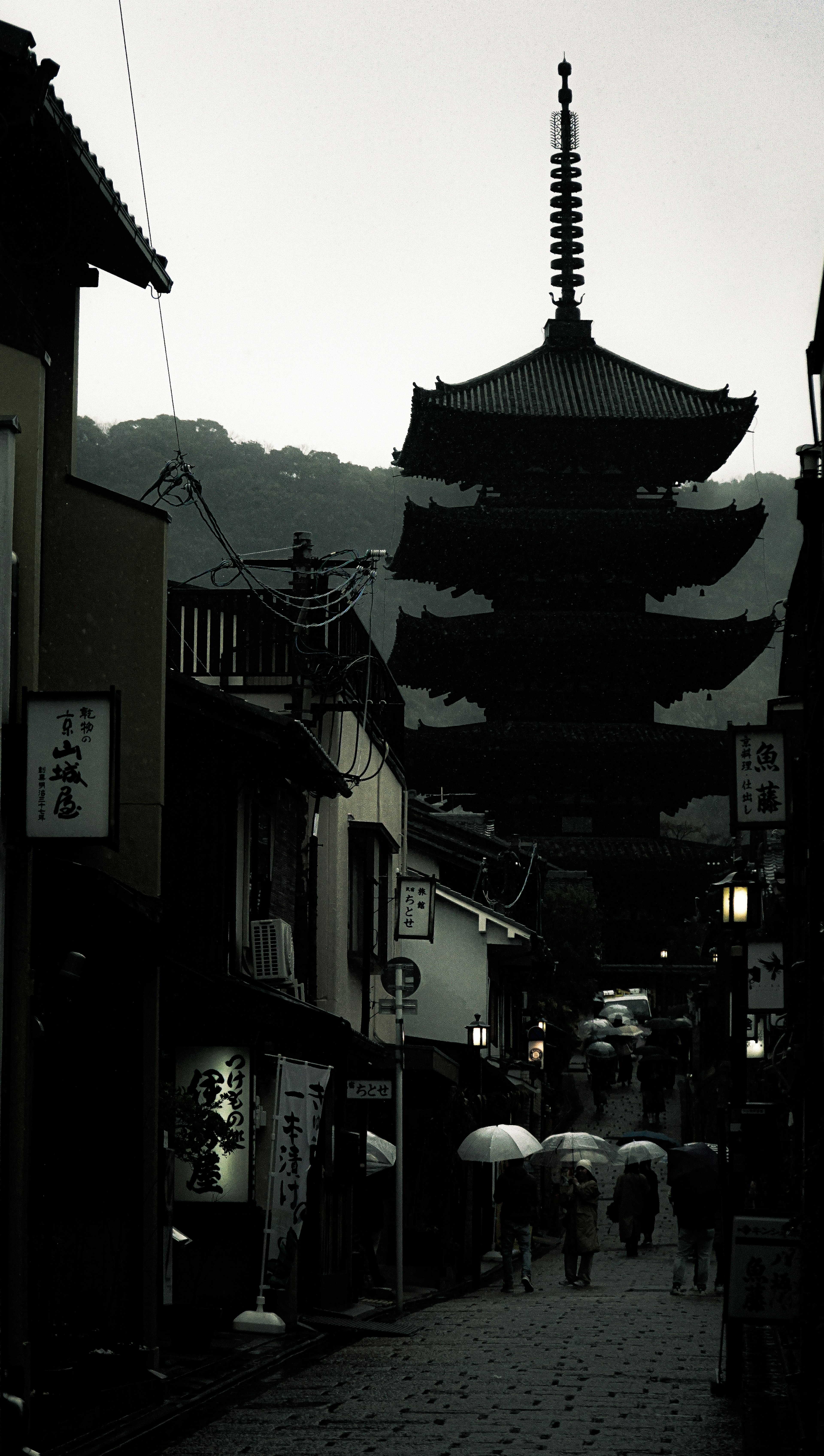 Silhouette di una pagoda a Kyoto con persone che tengono ombrelli in una giornata di pioggia