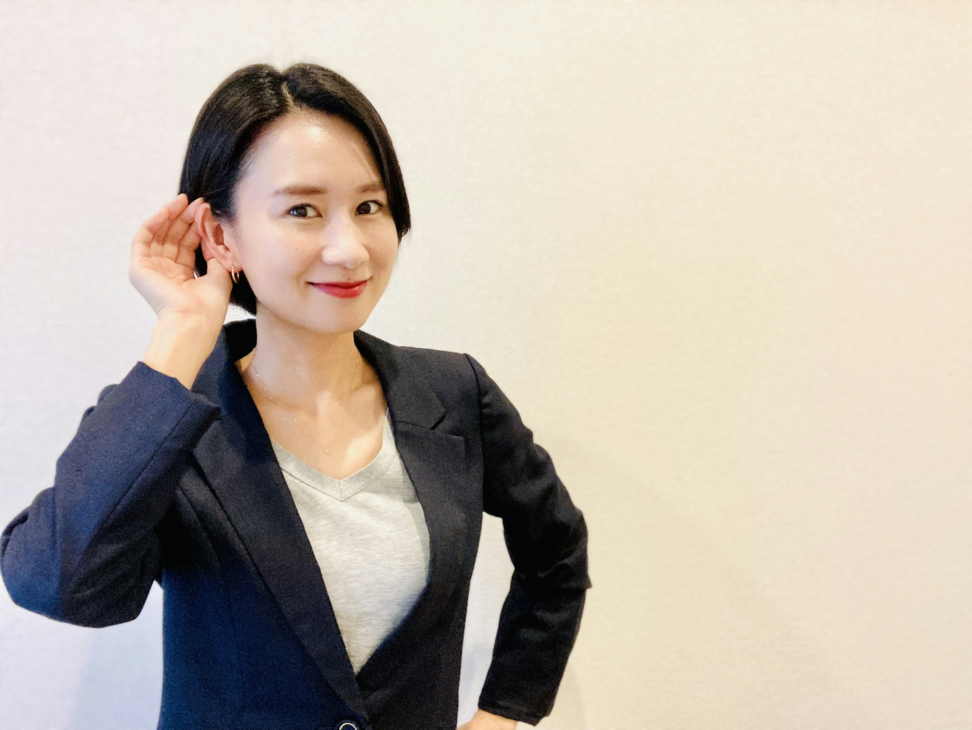 A woman in a business suit is posing with her hand to her ear