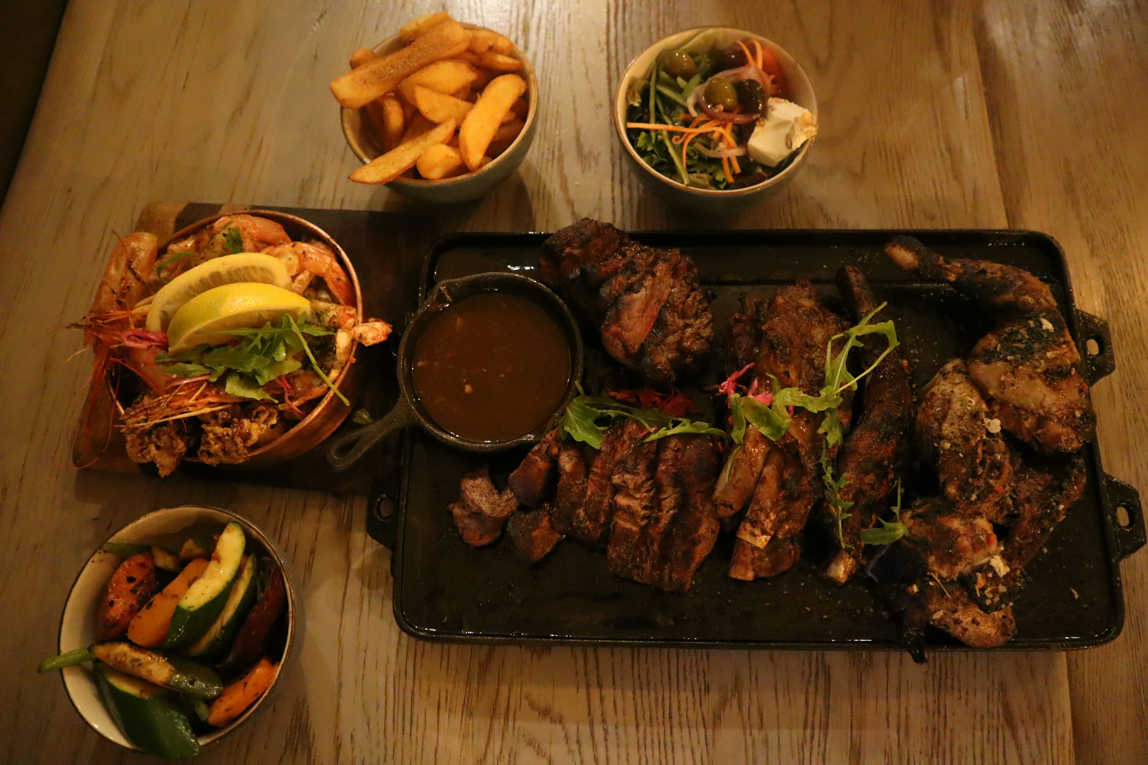 Plato de carne a la parrilla servido en una placa caliente con guarniciones de ensalada y papas fritas