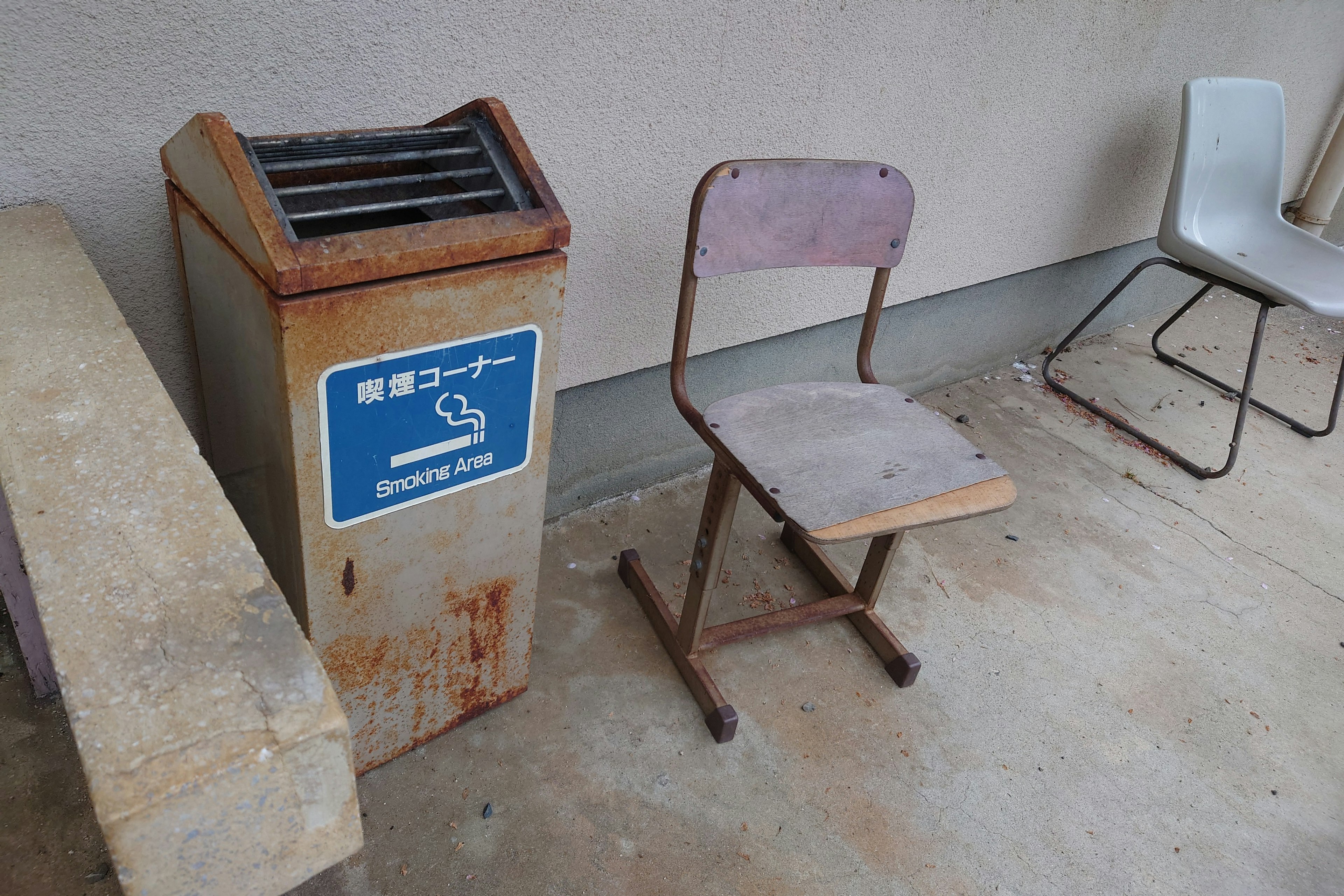 Viejo bote de basura oxidado con un letrero y una silla desgastada al lado