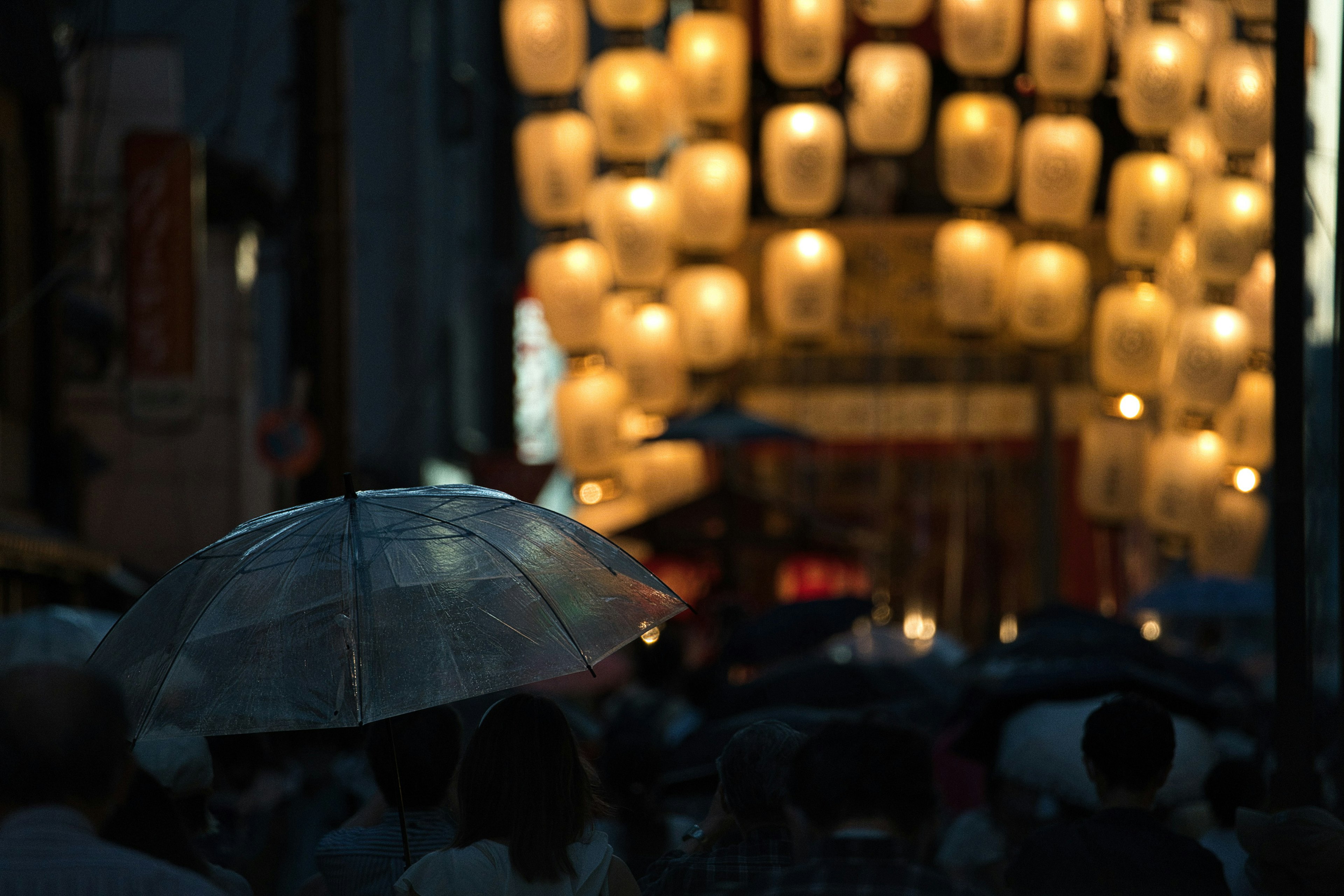 夜晚城市中人們手持傘，背景是發光的燈籠