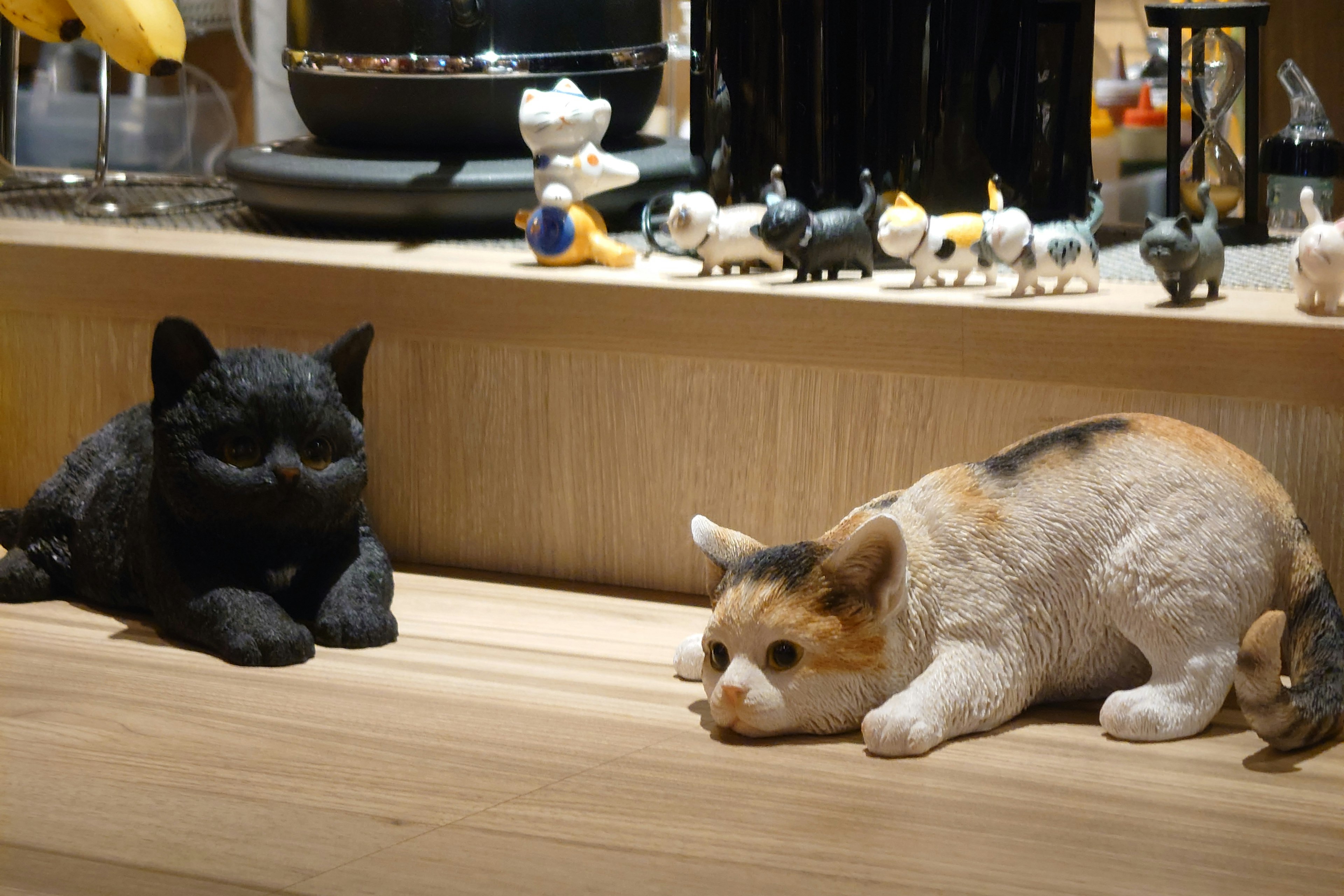 Black cat and calico cat figurines on a wooden table