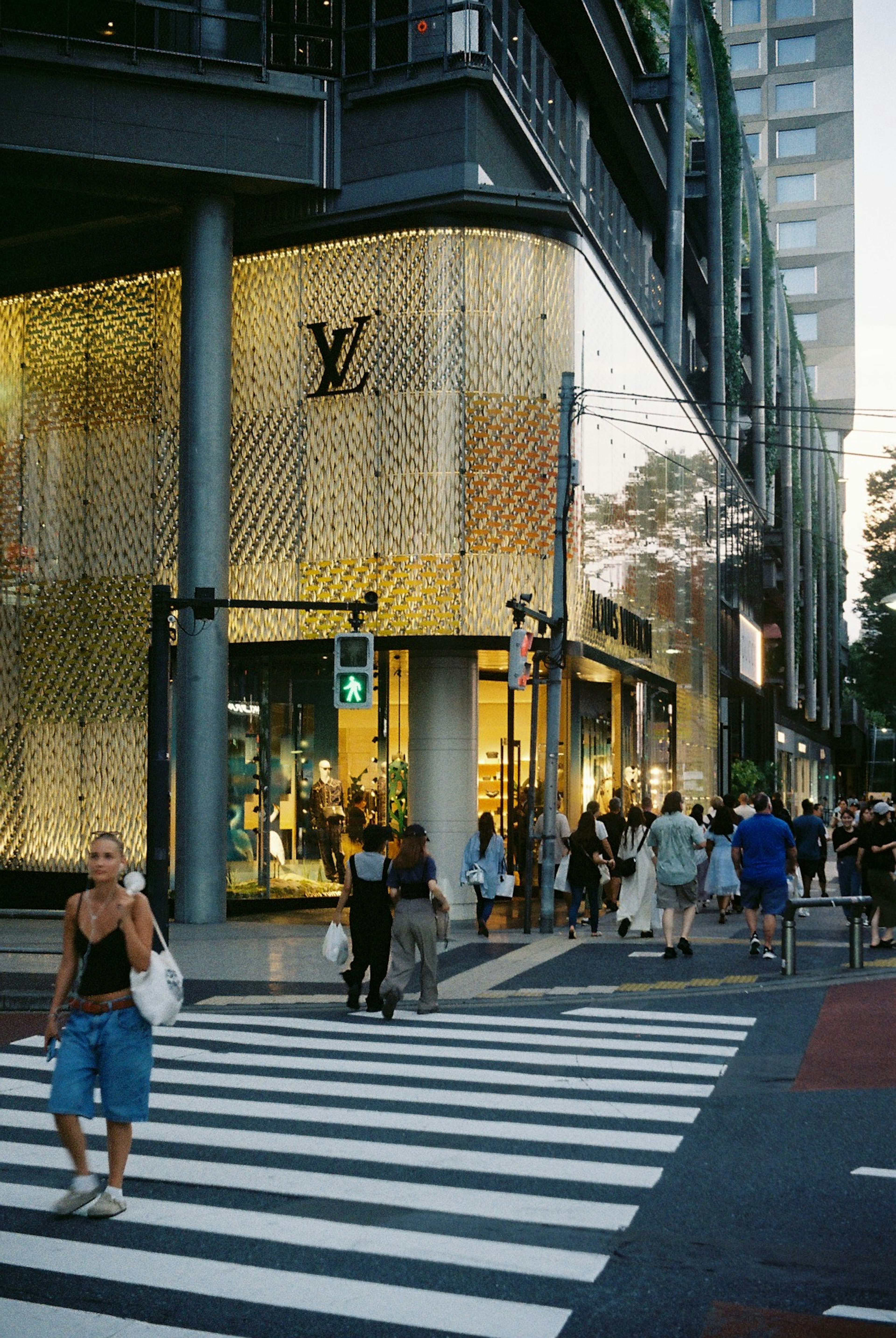 Scene at a crosswalk featuring a Louis Vuitton store with pedestrians