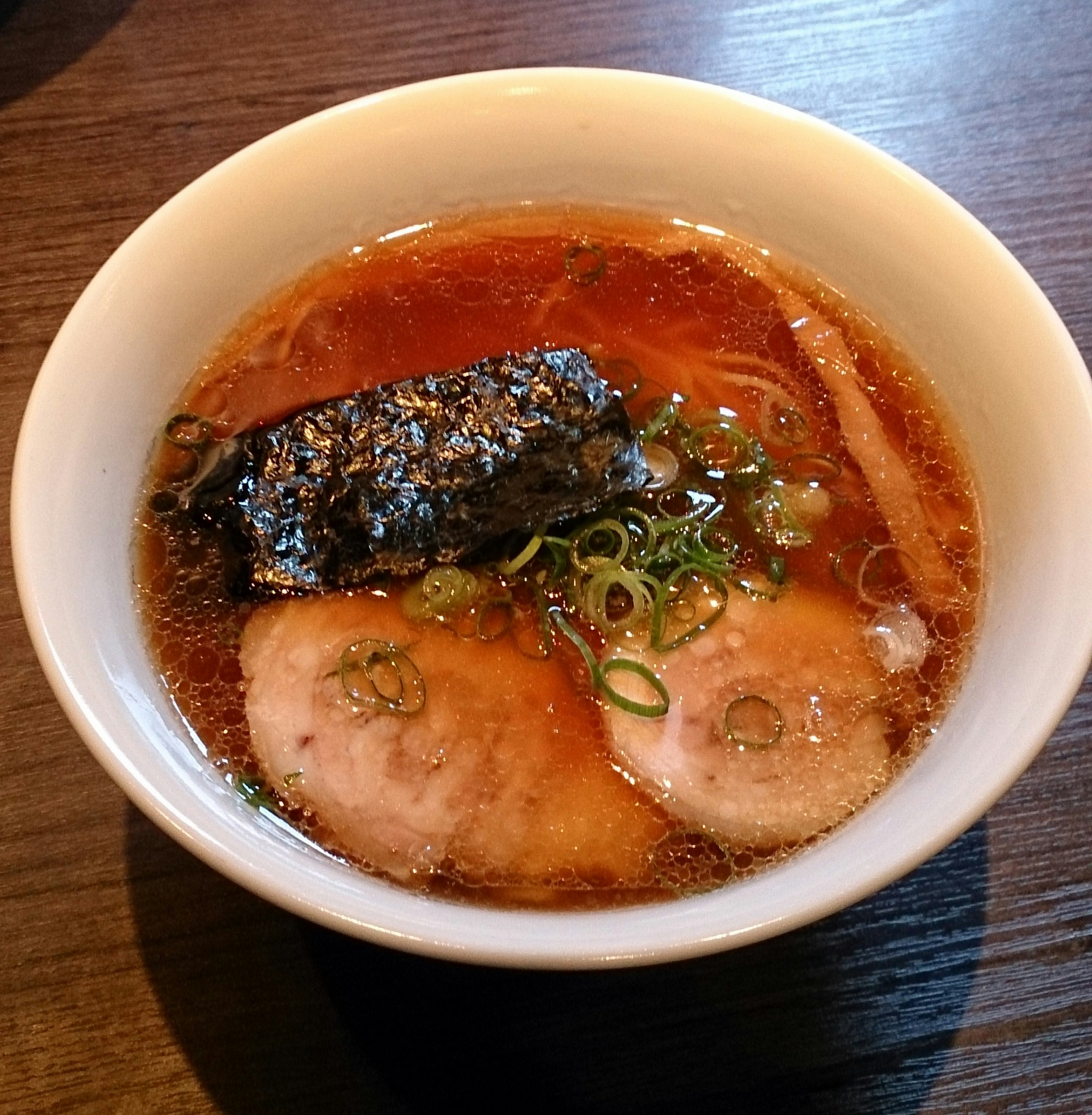 A delicious bowl of ramen featuring sliced pork, green onions, and seaweed