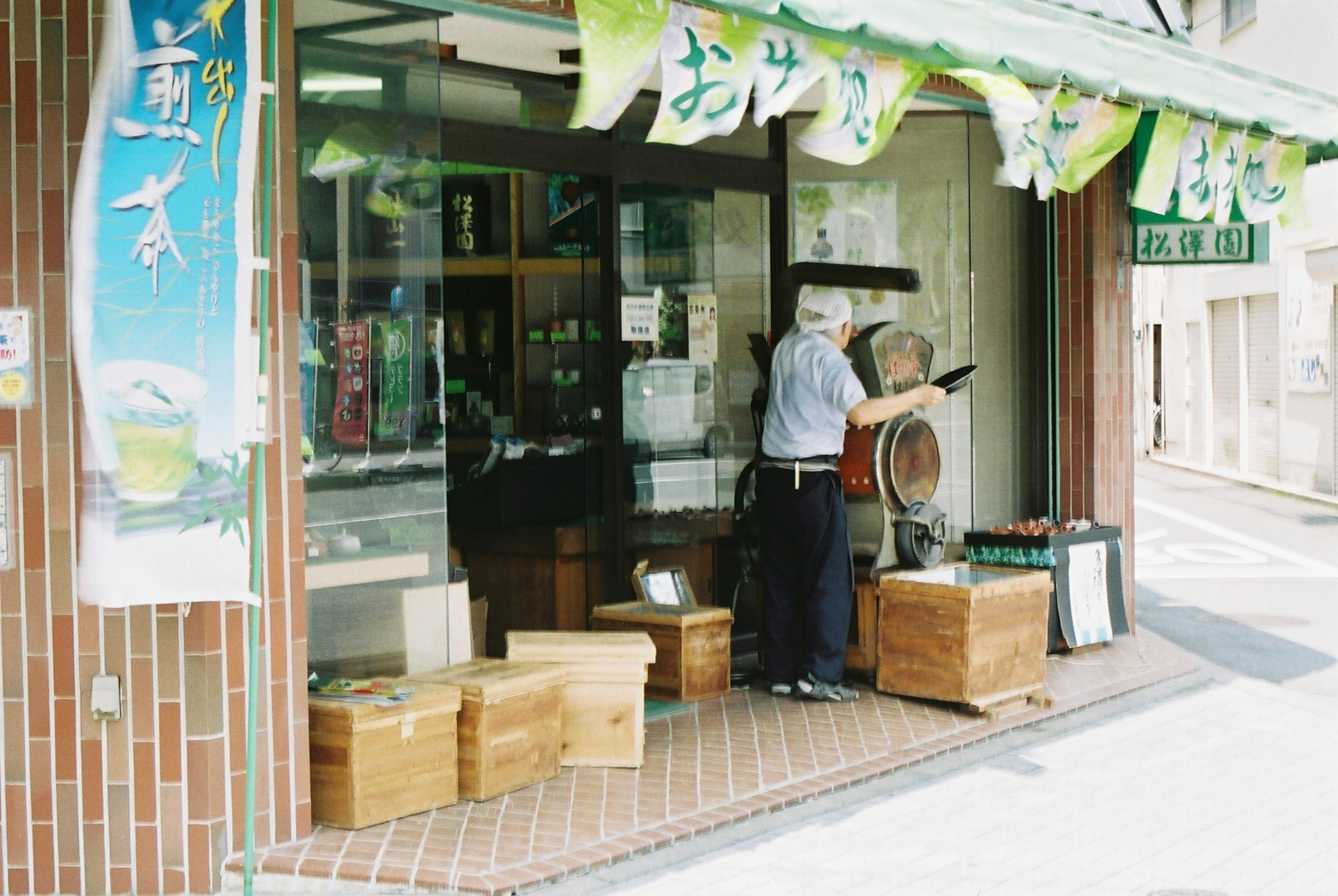 伝統的な日本の店舗の外観で、木箱が並べられた前面に店主が立っている