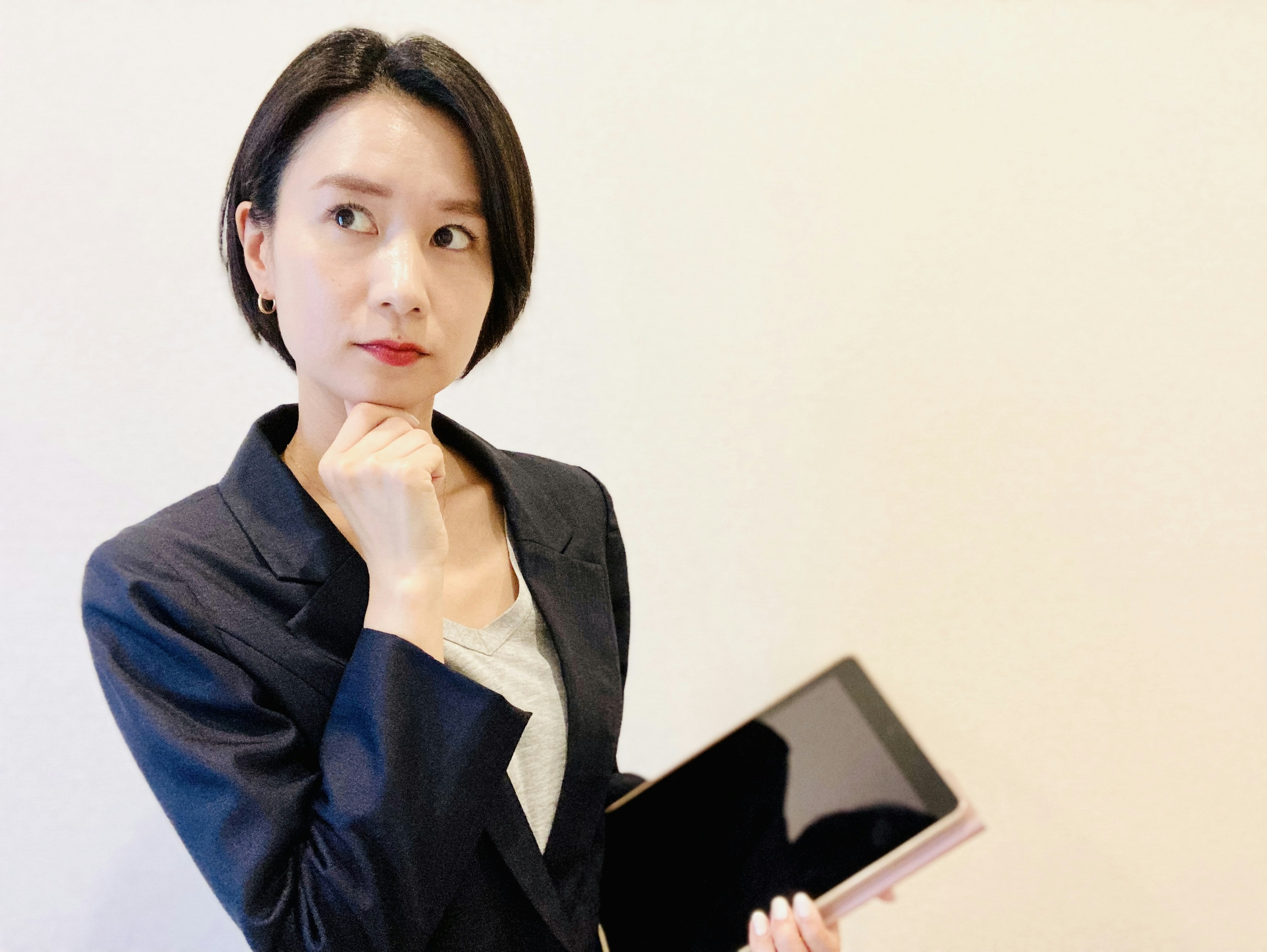 A woman in a business suit holding a tablet looking thoughtful