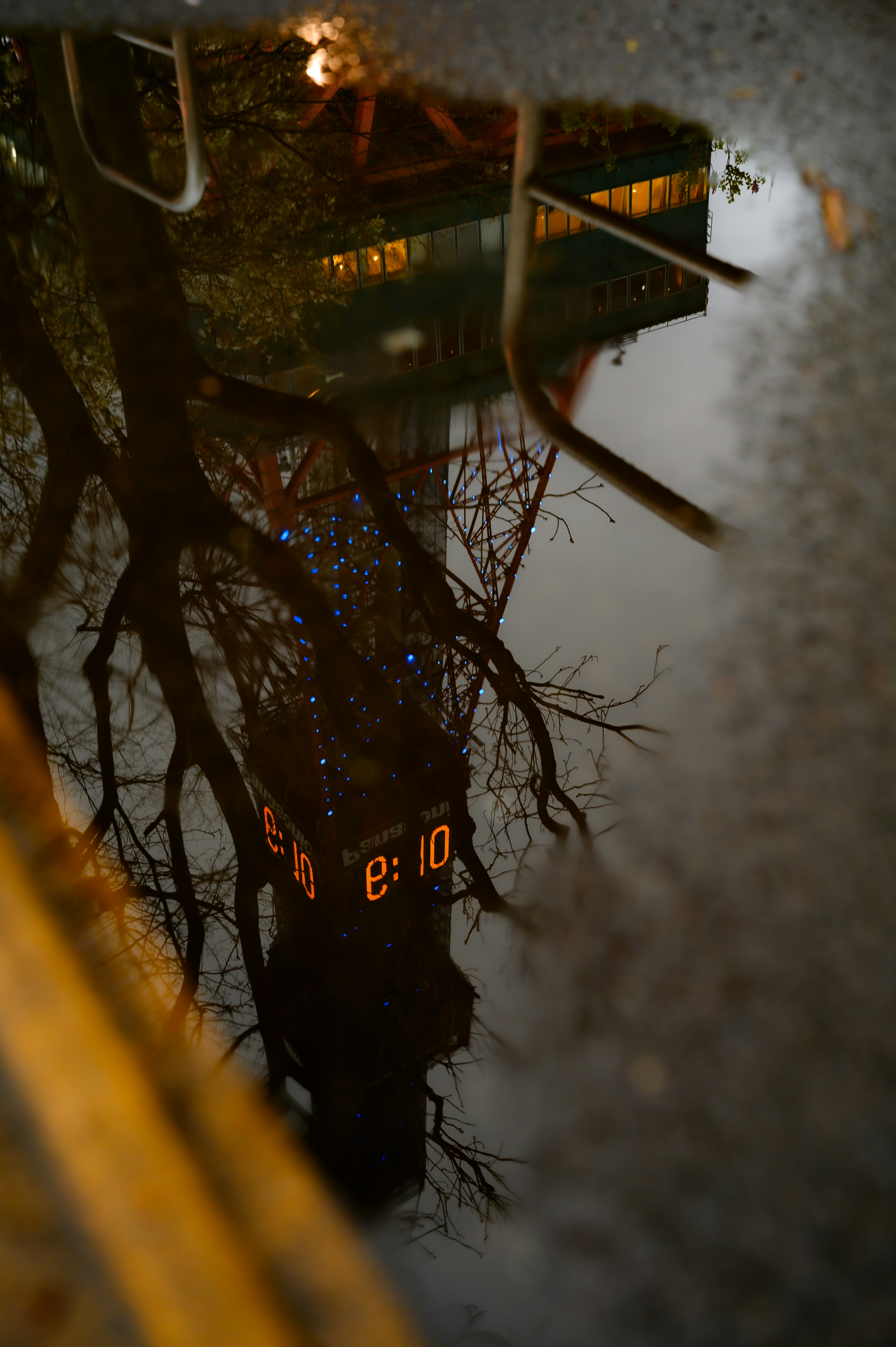 Refleksi menara jam di genangan air dengan pohon di sekitarnya