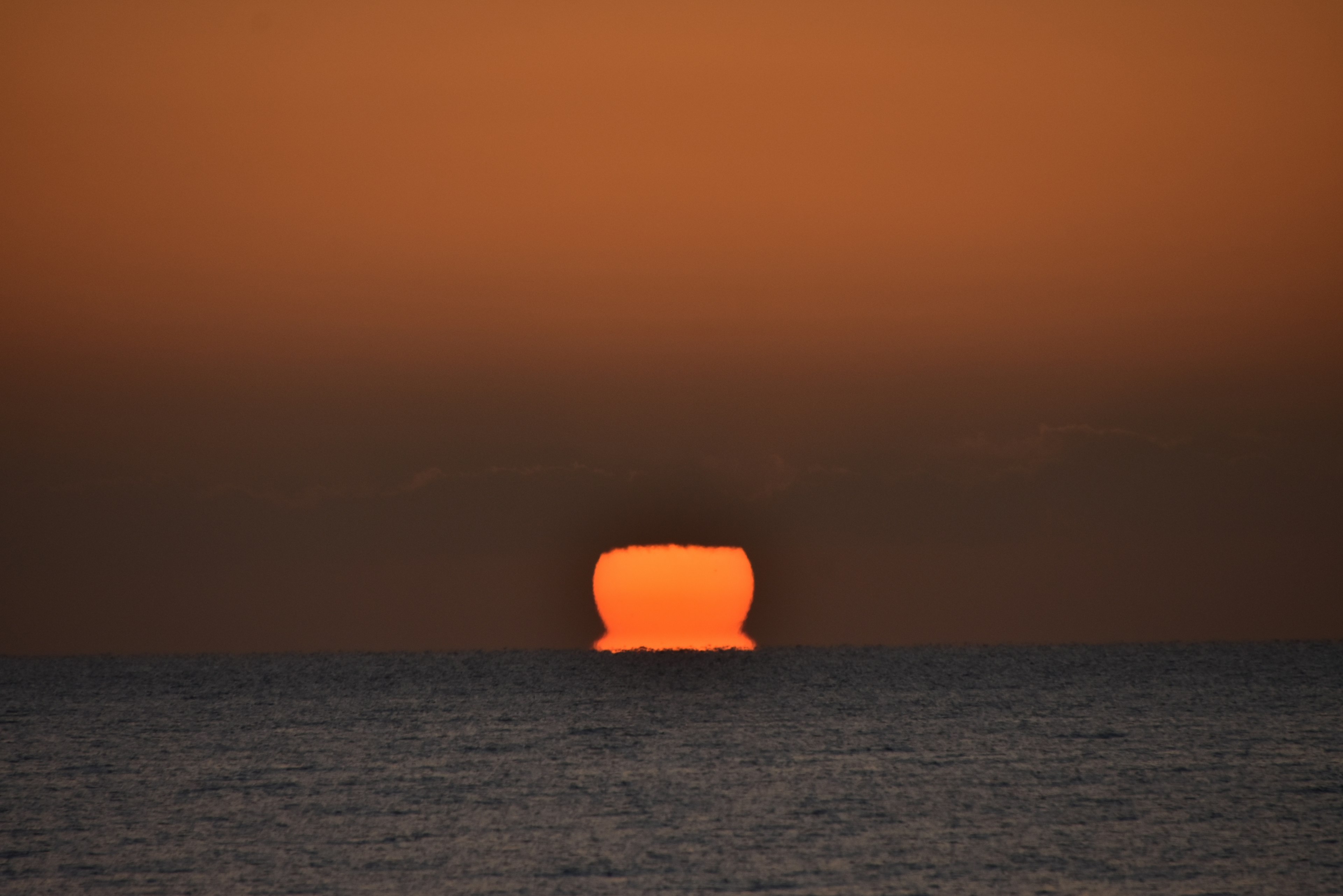 Large orange sun setting on the horizon over the ocean