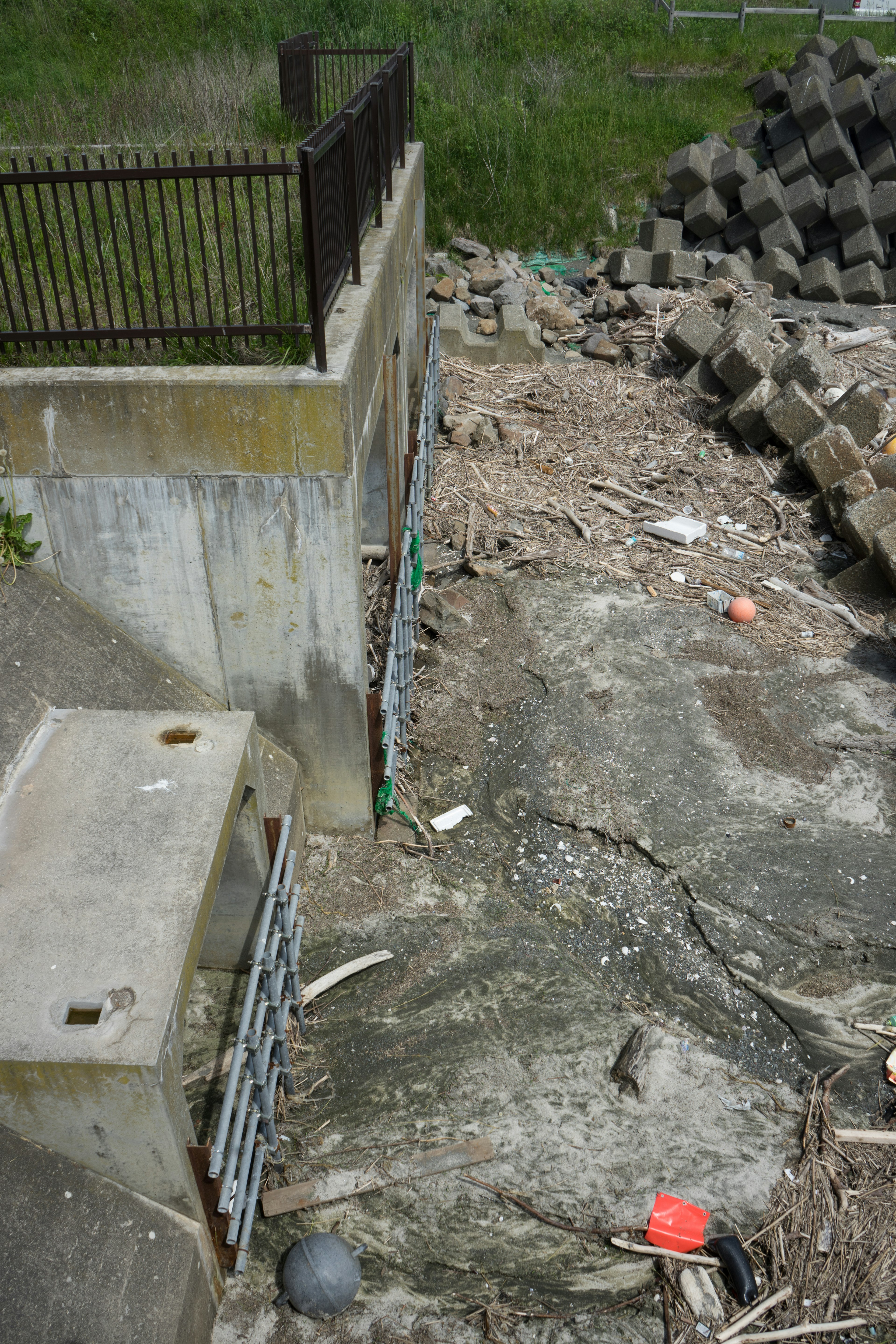 Structure en béton avec des débris et une zone herbeuse montrant des déchets éparpillés et des blocs de béton