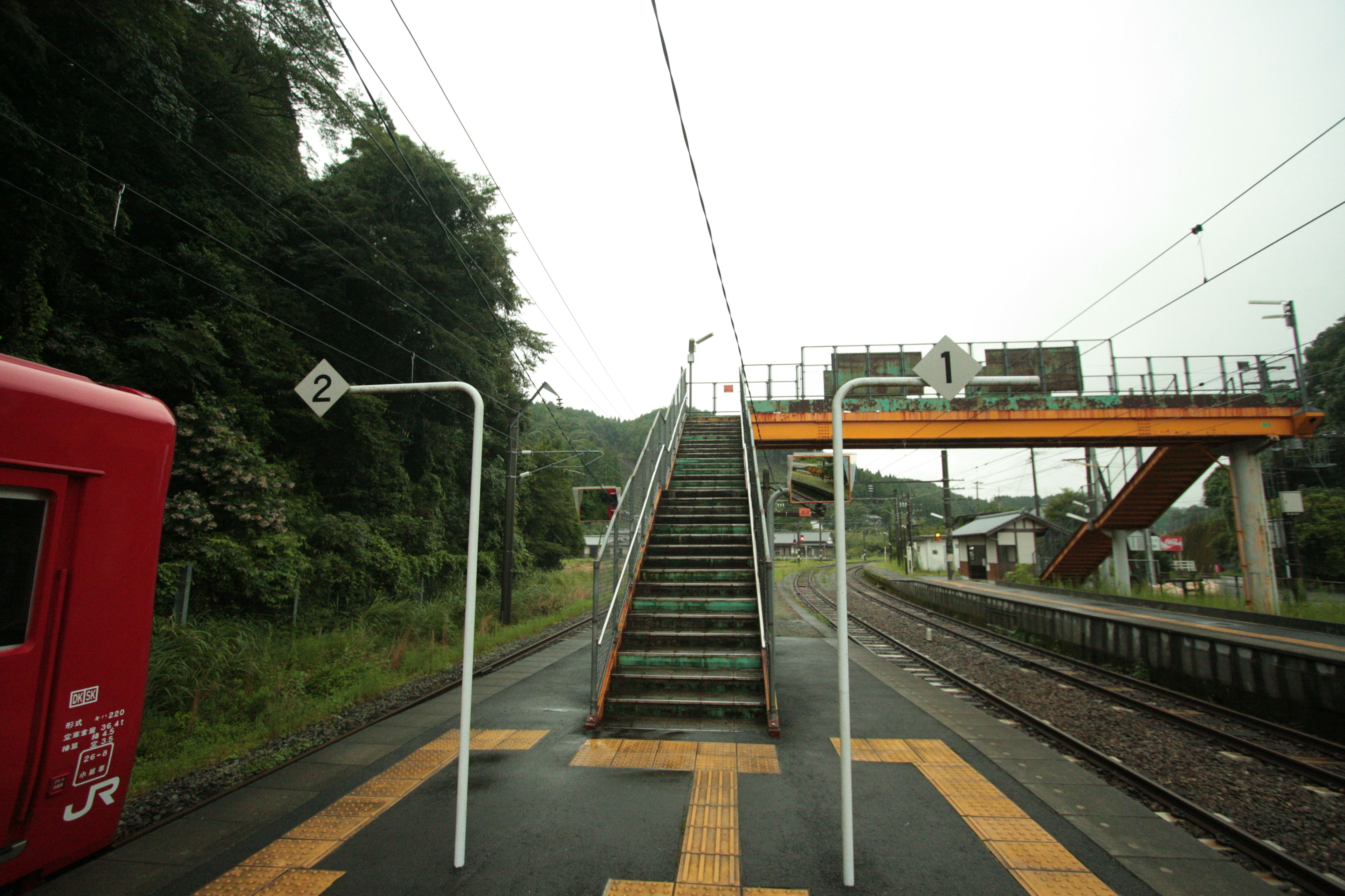 Blick auf einen Bahnhof mit einem parkenden roten Zug Treppen, die zur Plattform führen