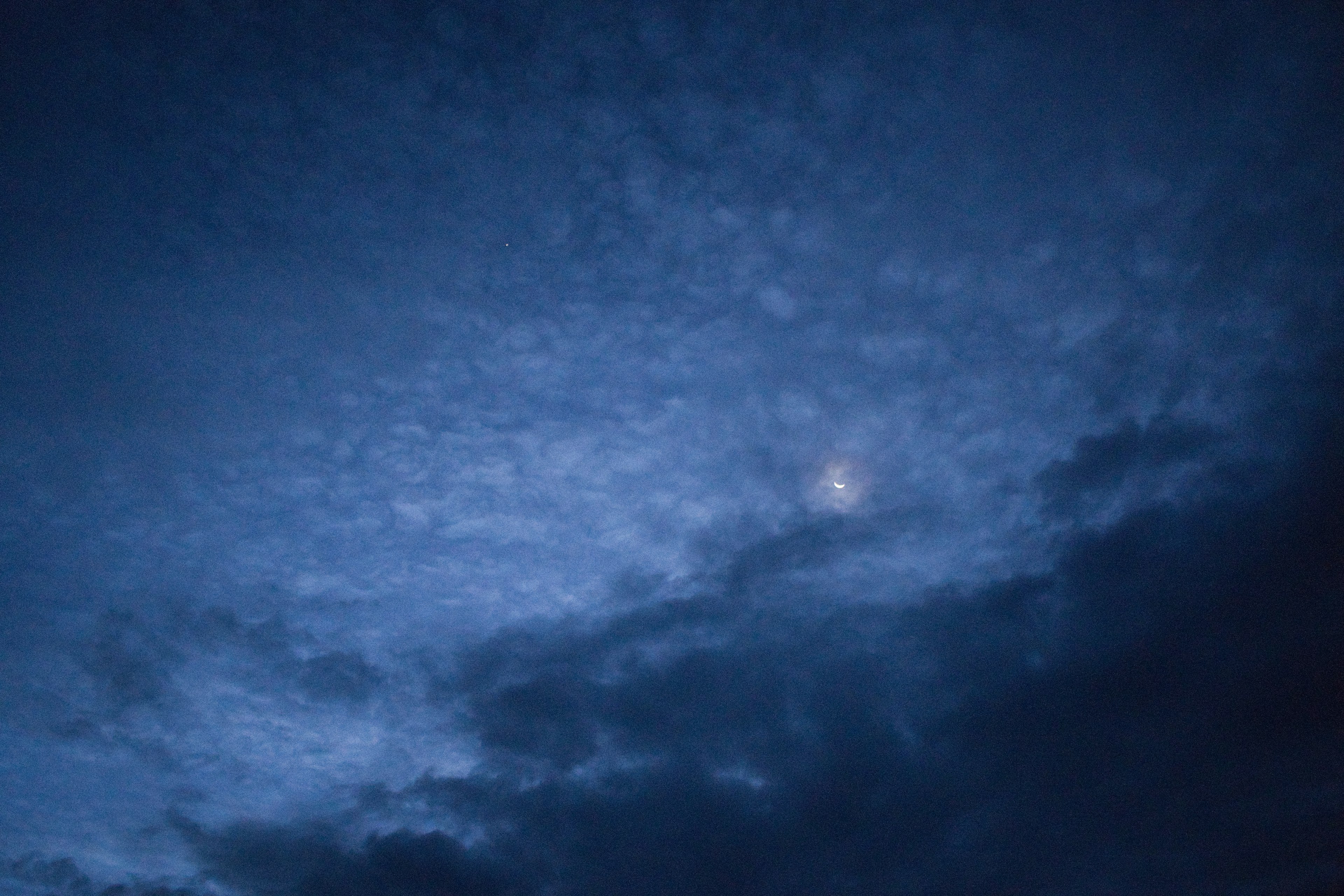 暗い青空に浮かぶ雲と月の一部