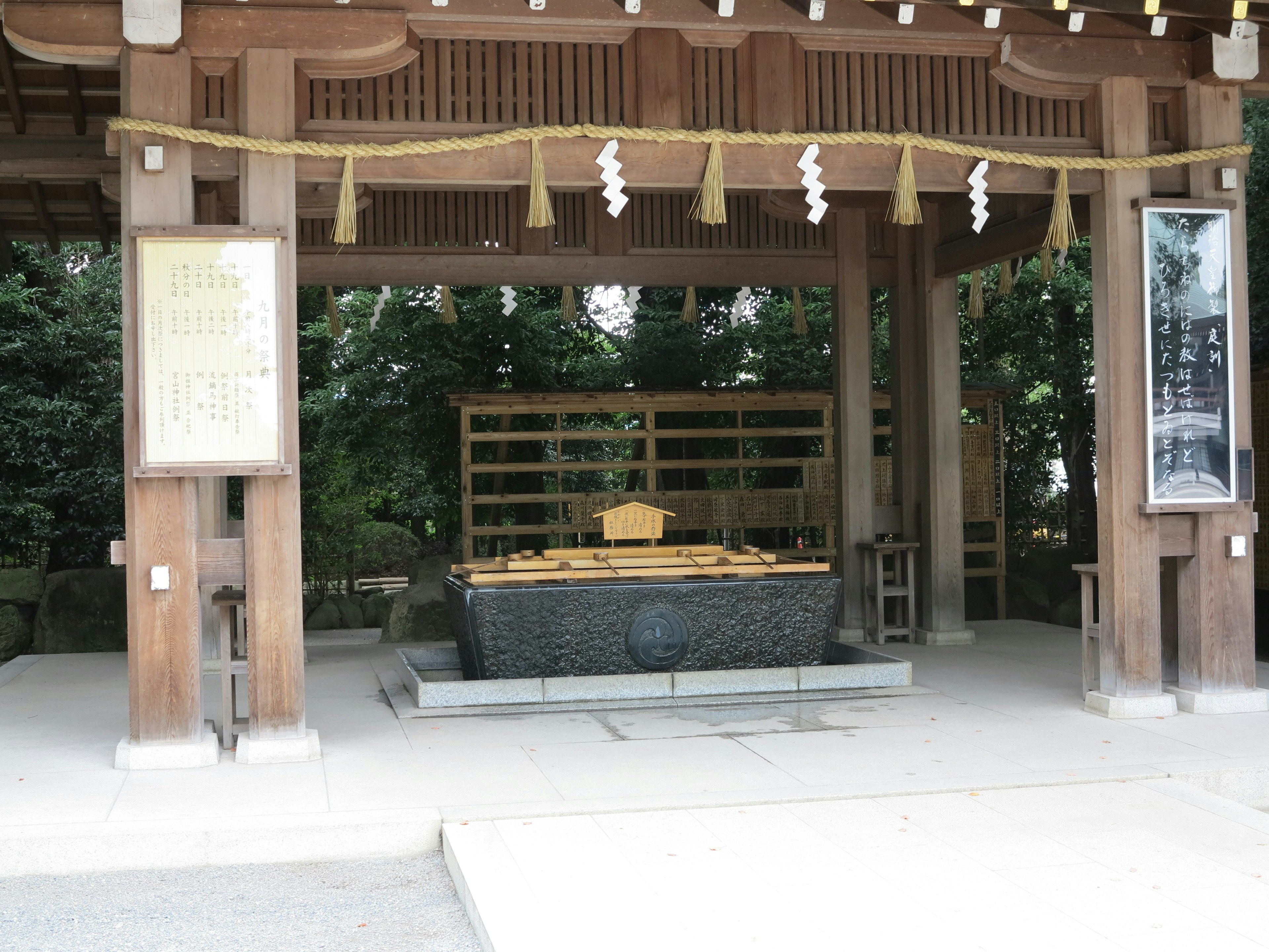 A roofed structure featuring a water basin at a shrine with wooden and stone elements