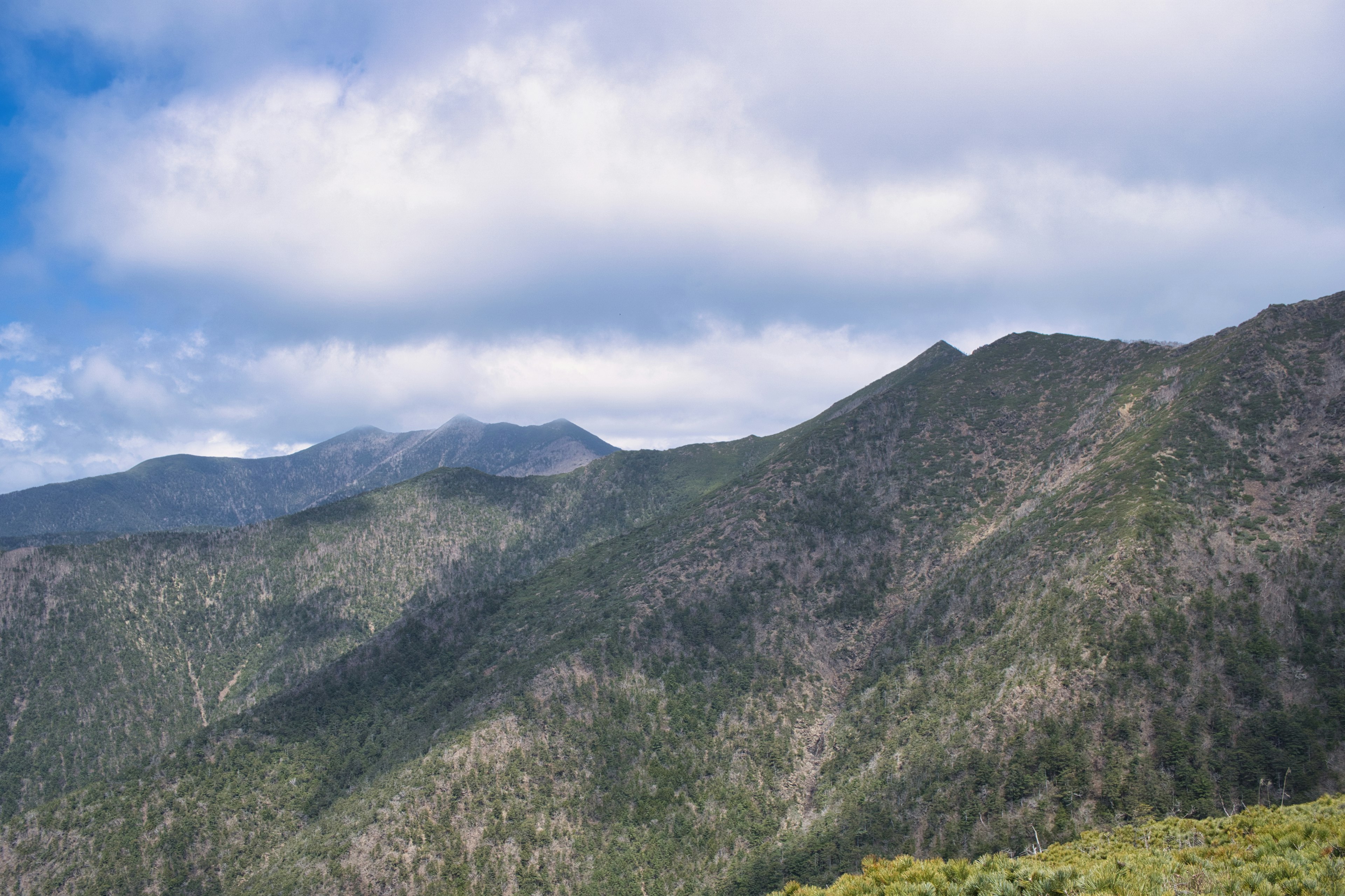 Paisaje montañoso con cielo azul y nubes vegetación verde cubriendo las laderas