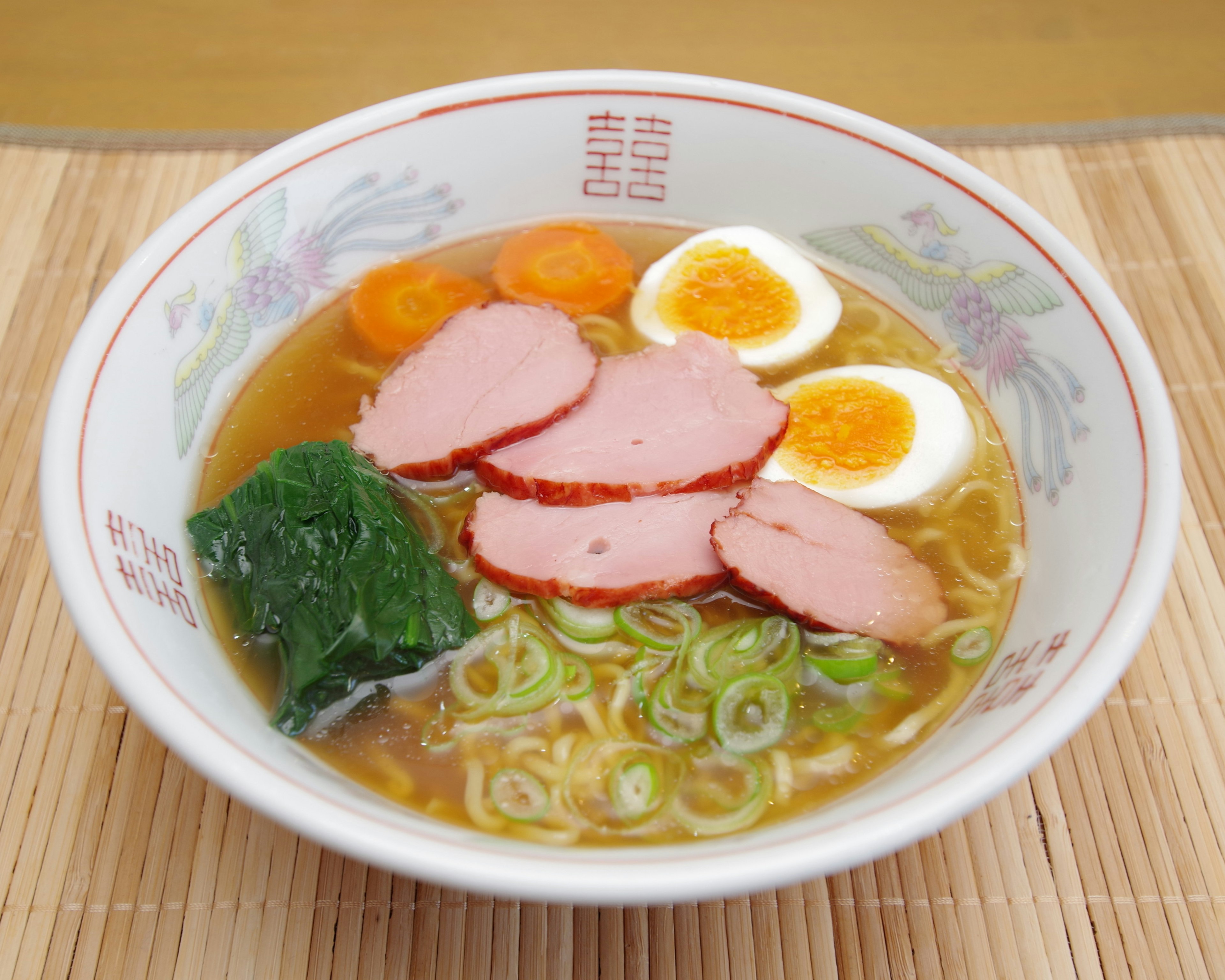 A delicious bowl of ramen featuring sliced chashu, soft-boiled eggs, green onions, seaweed, and carrots