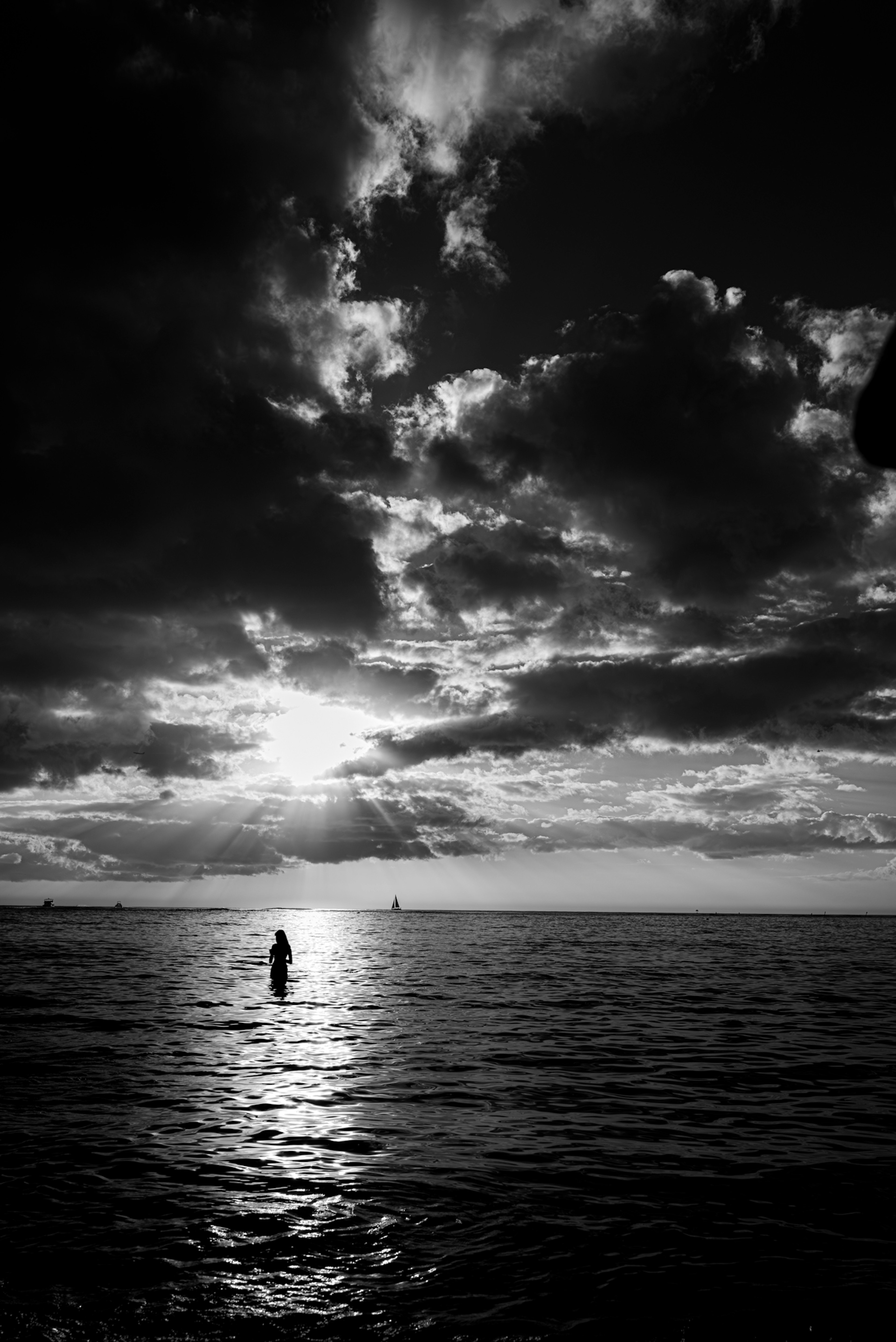 Silhouette einer Person, die im Meer steht, mit dramatischen Wolken in Schwarz-Weiß