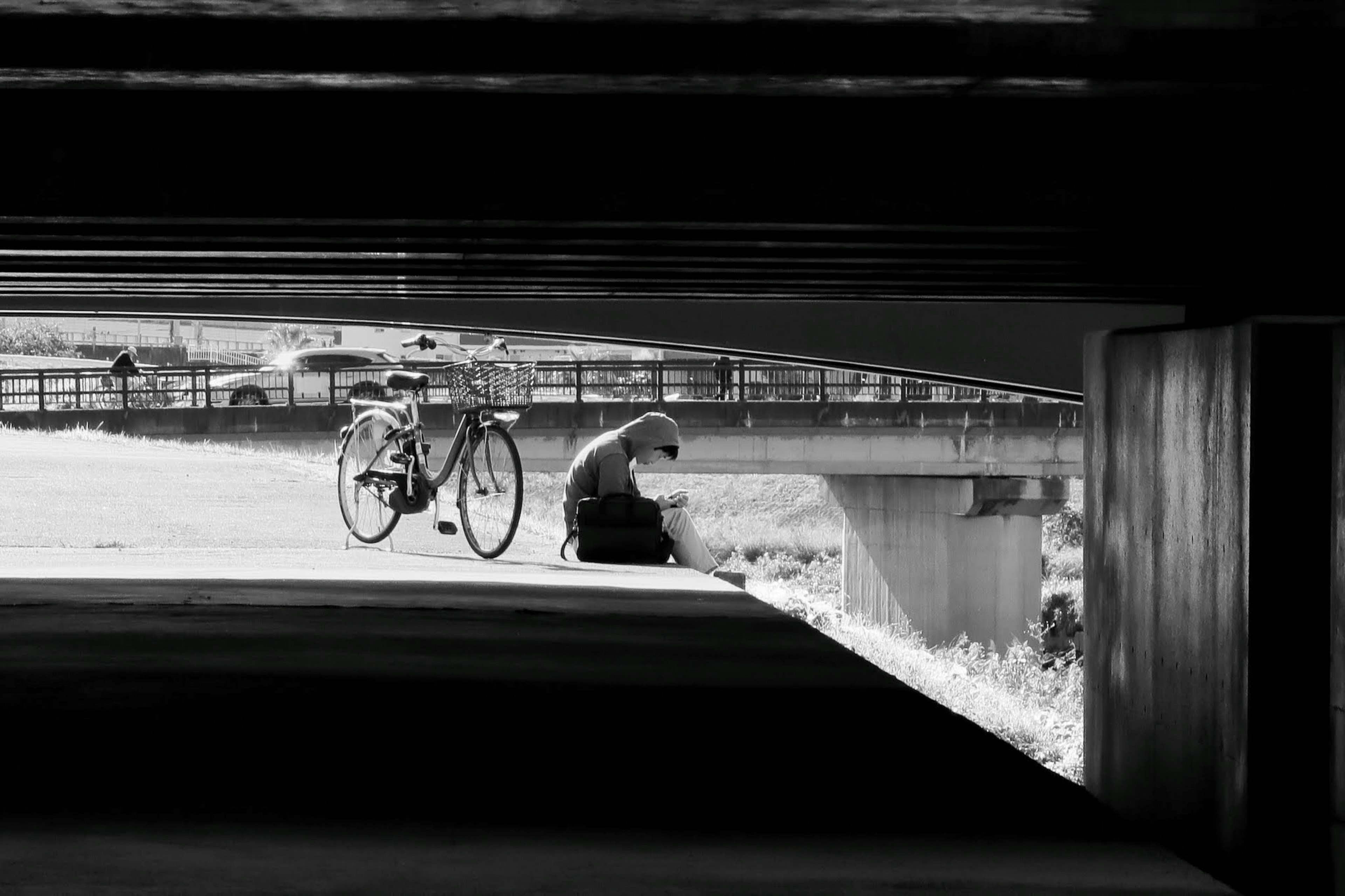 A person sitting by a bicycle under a bridge