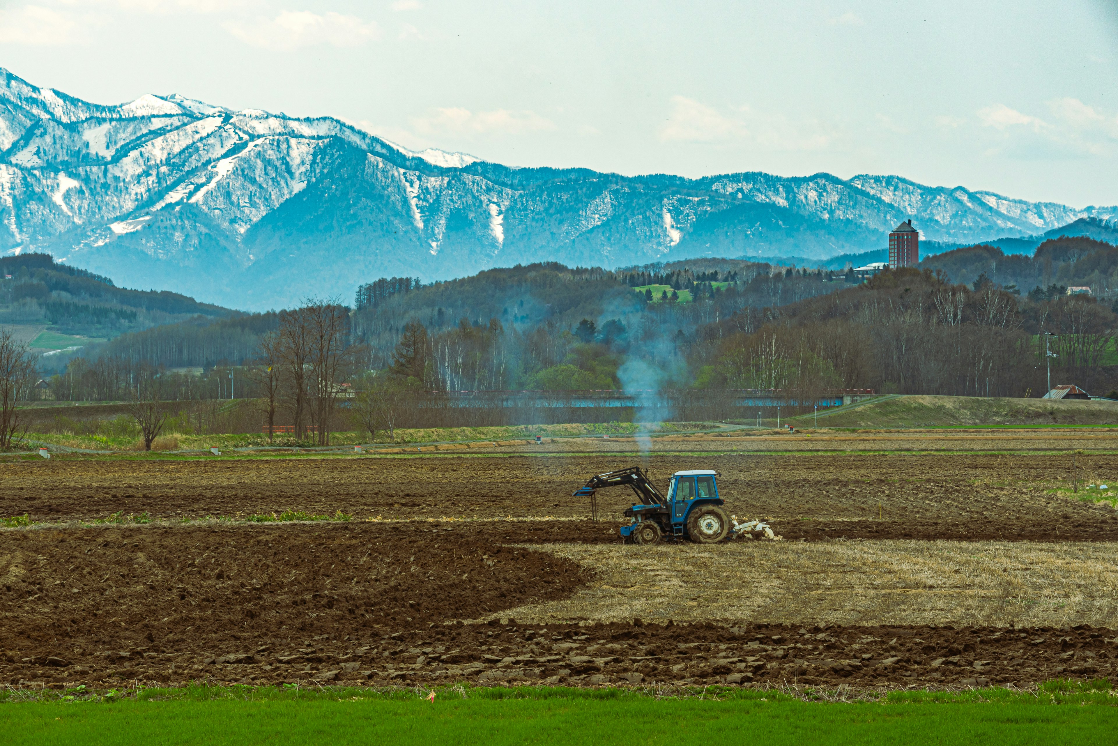 Tractor arando un campo con montañas nevadas al fondo