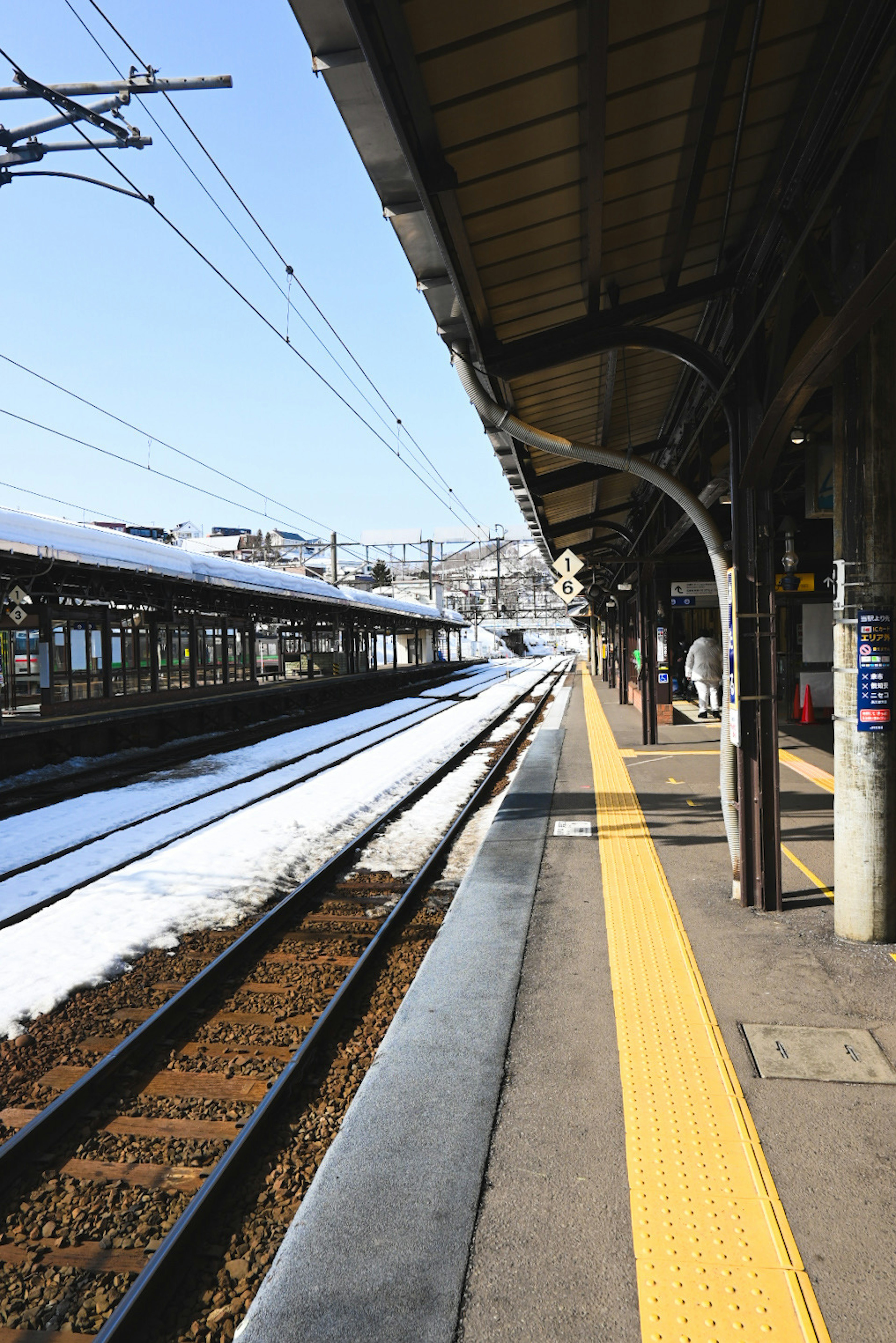 Escena invernal de una plataforma de estación de tren con rieles cubiertos de nieve y cielo azul