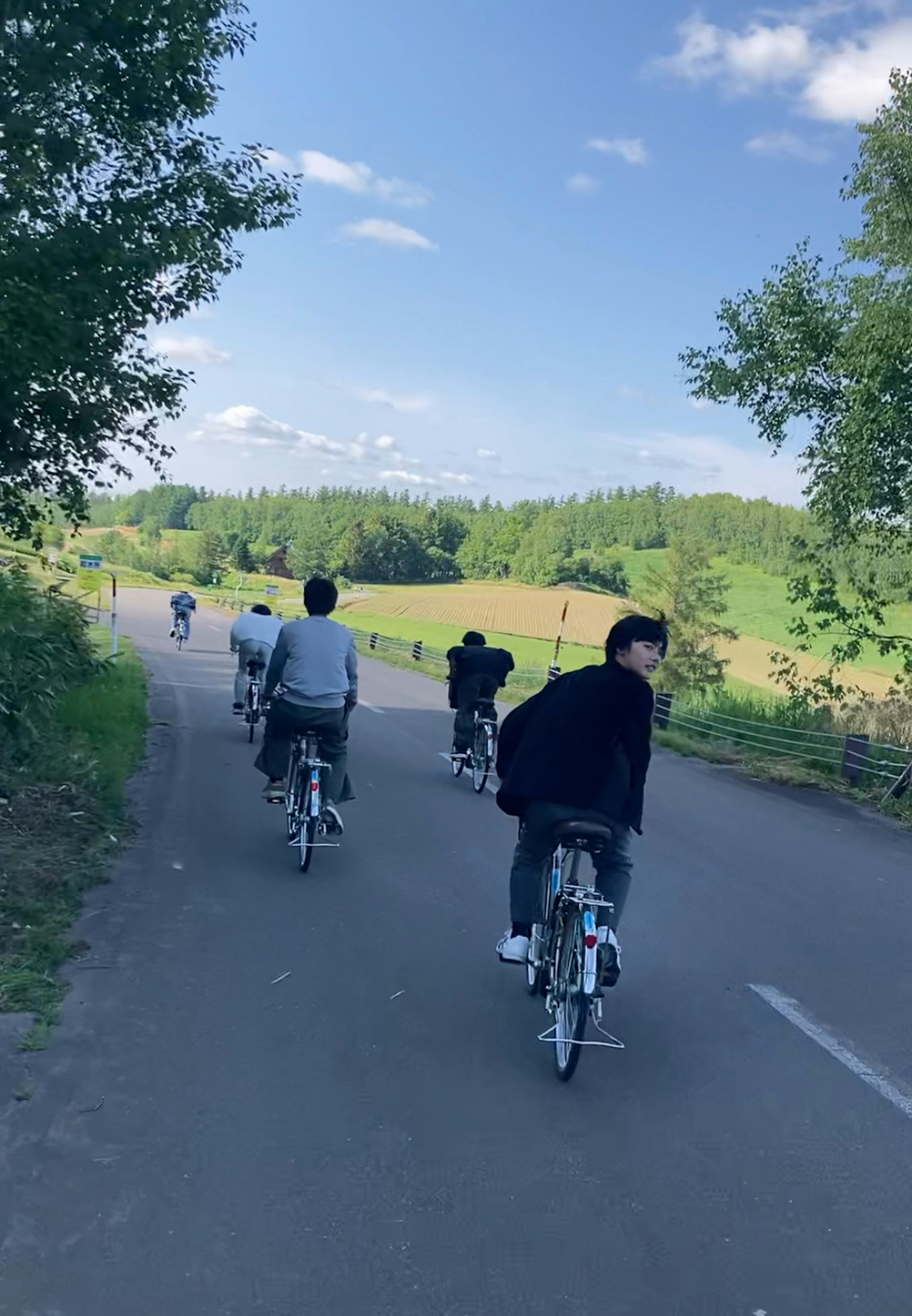 青空の下で自転車に乗る人々の後ろ姿の風景