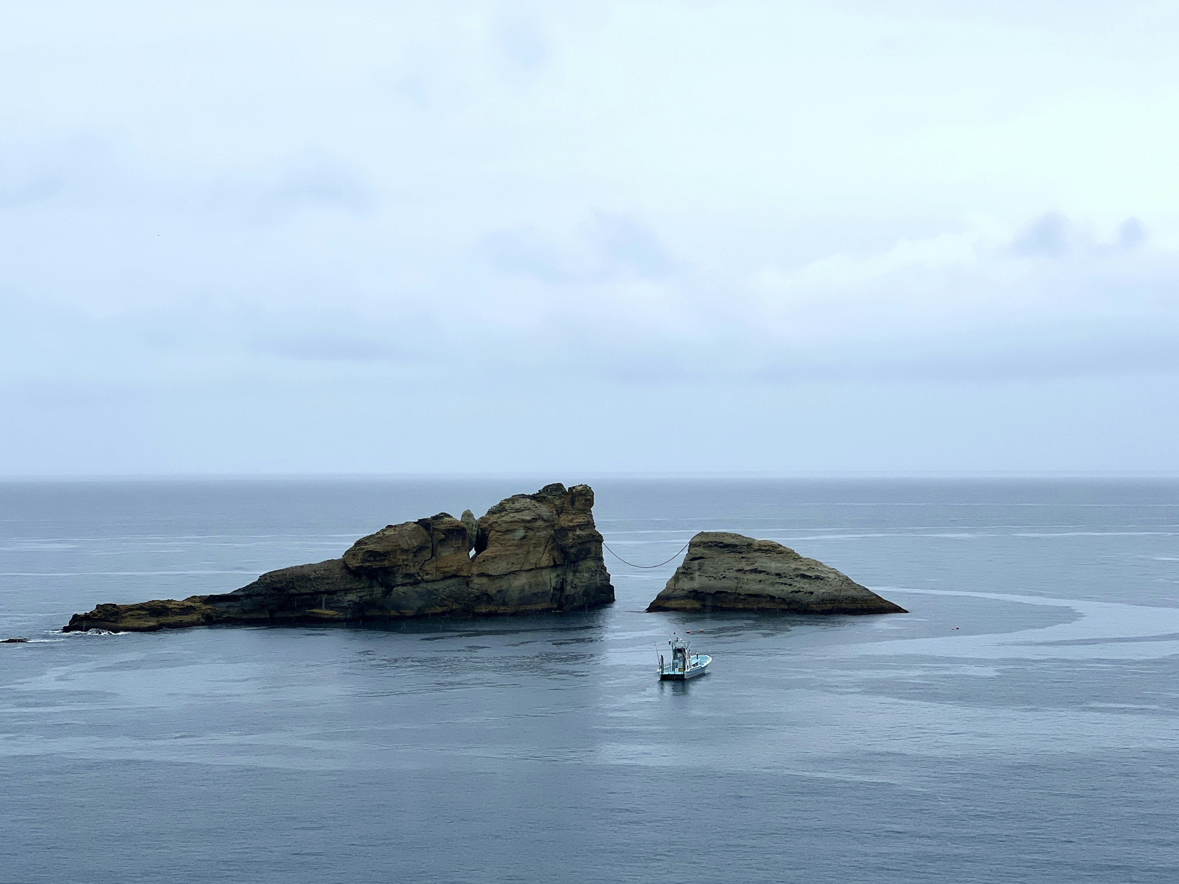 静かな海に浮かぶ二つの岩と小さな船