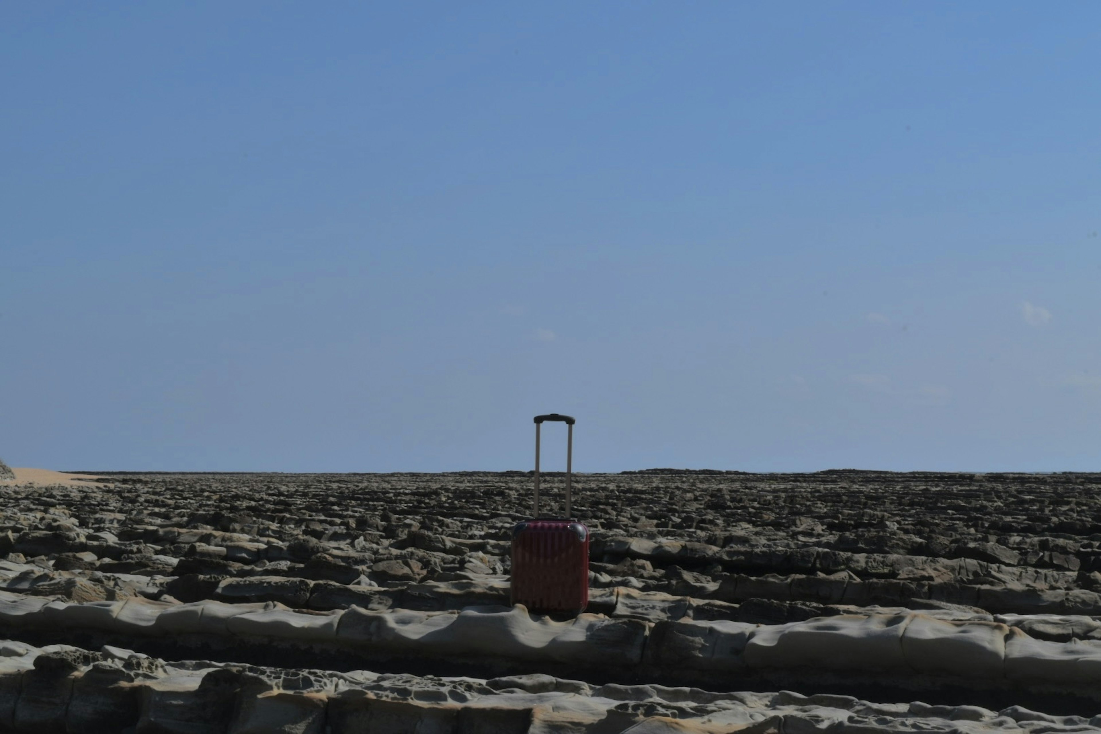 A small structure in a vast landscape with a clear blue sky and a prominent object on the ground