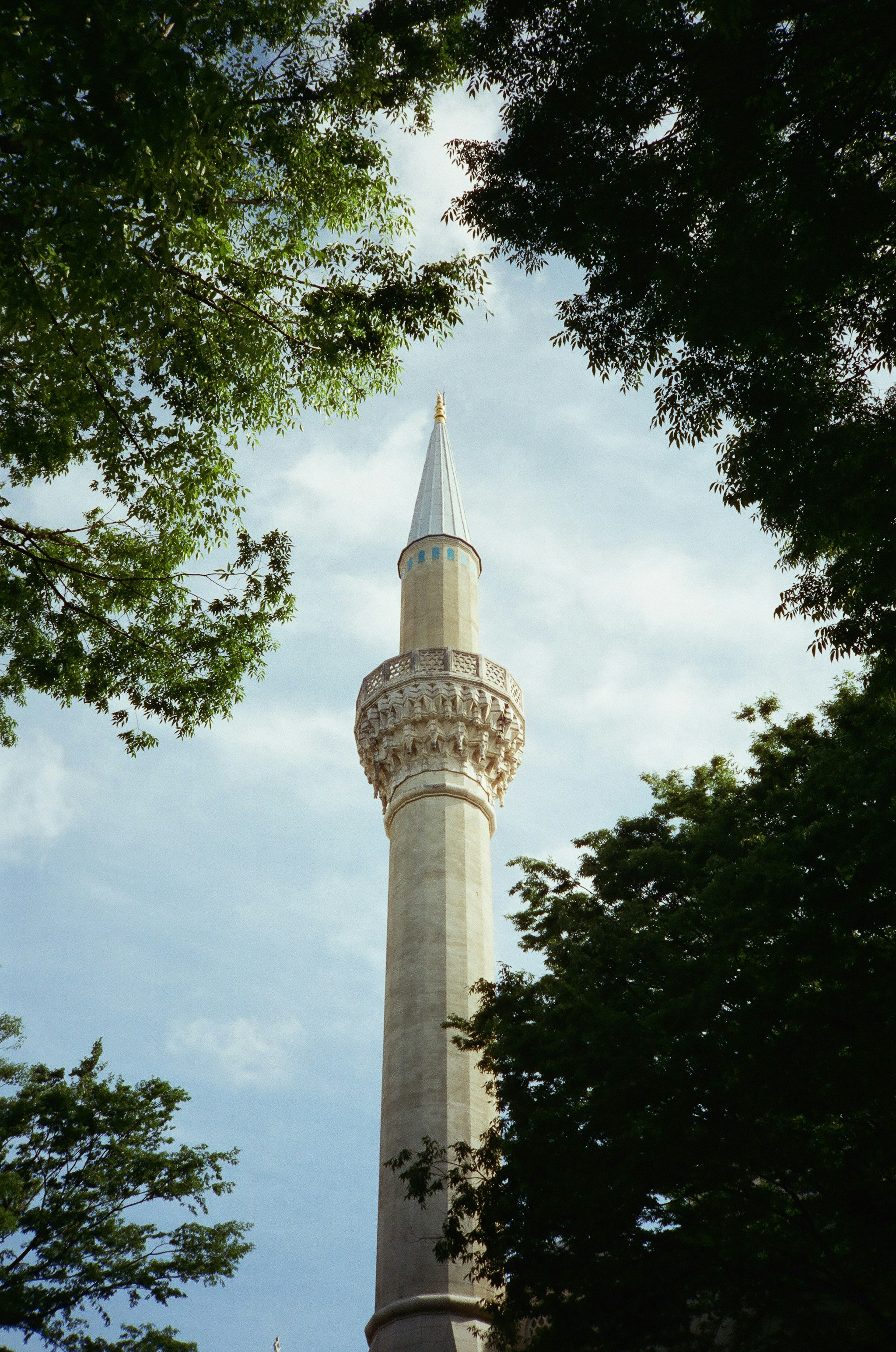 Alto minareto contro un cielo blu incorniciato da alberi verdi