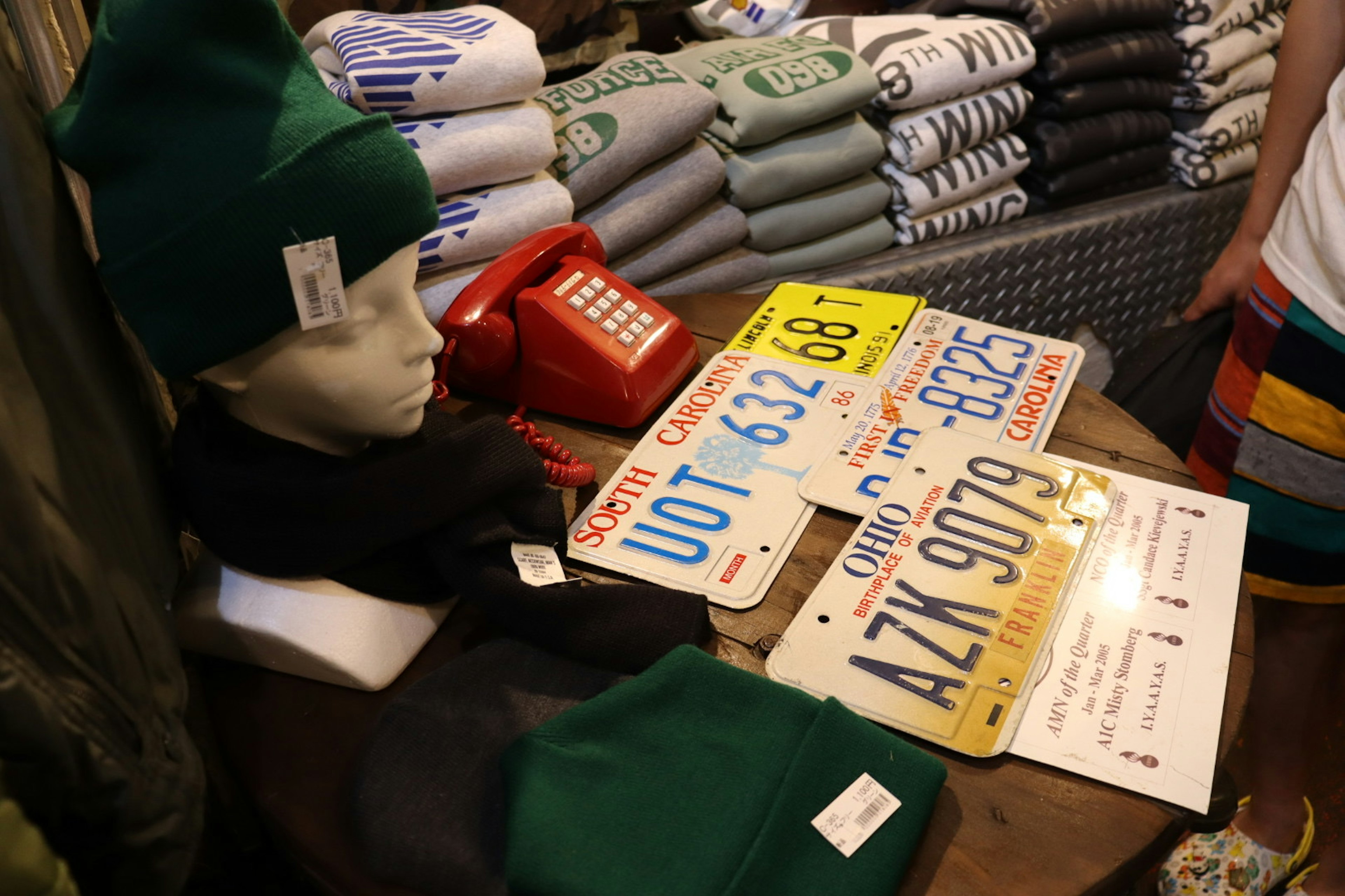 A mannequin wearing a green hat with colorful license plates displayed in a shop