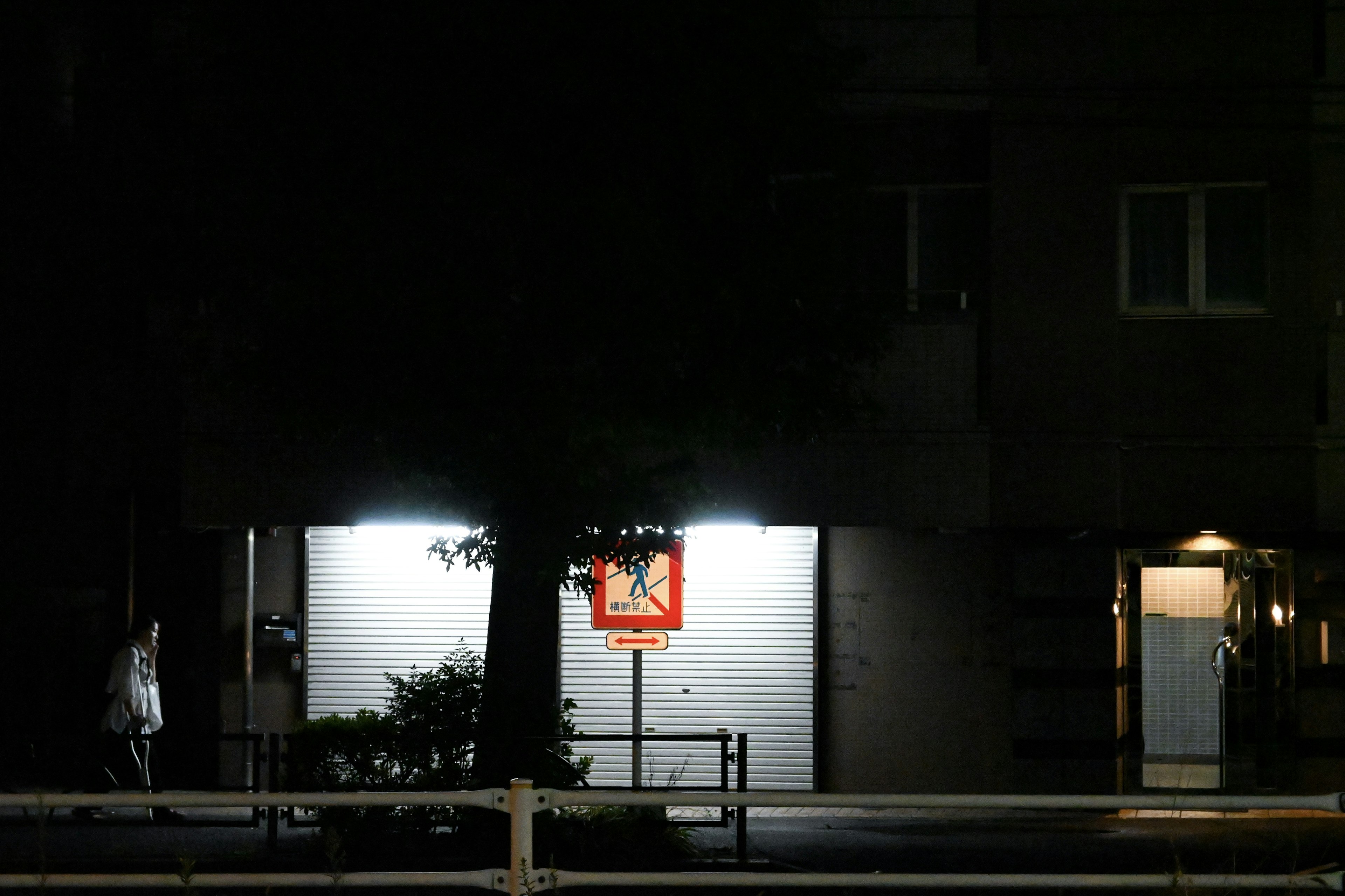 Ein beleuchteter Basketballkorb in der Nacht vor einem Gebäude mit einer Person, die geht