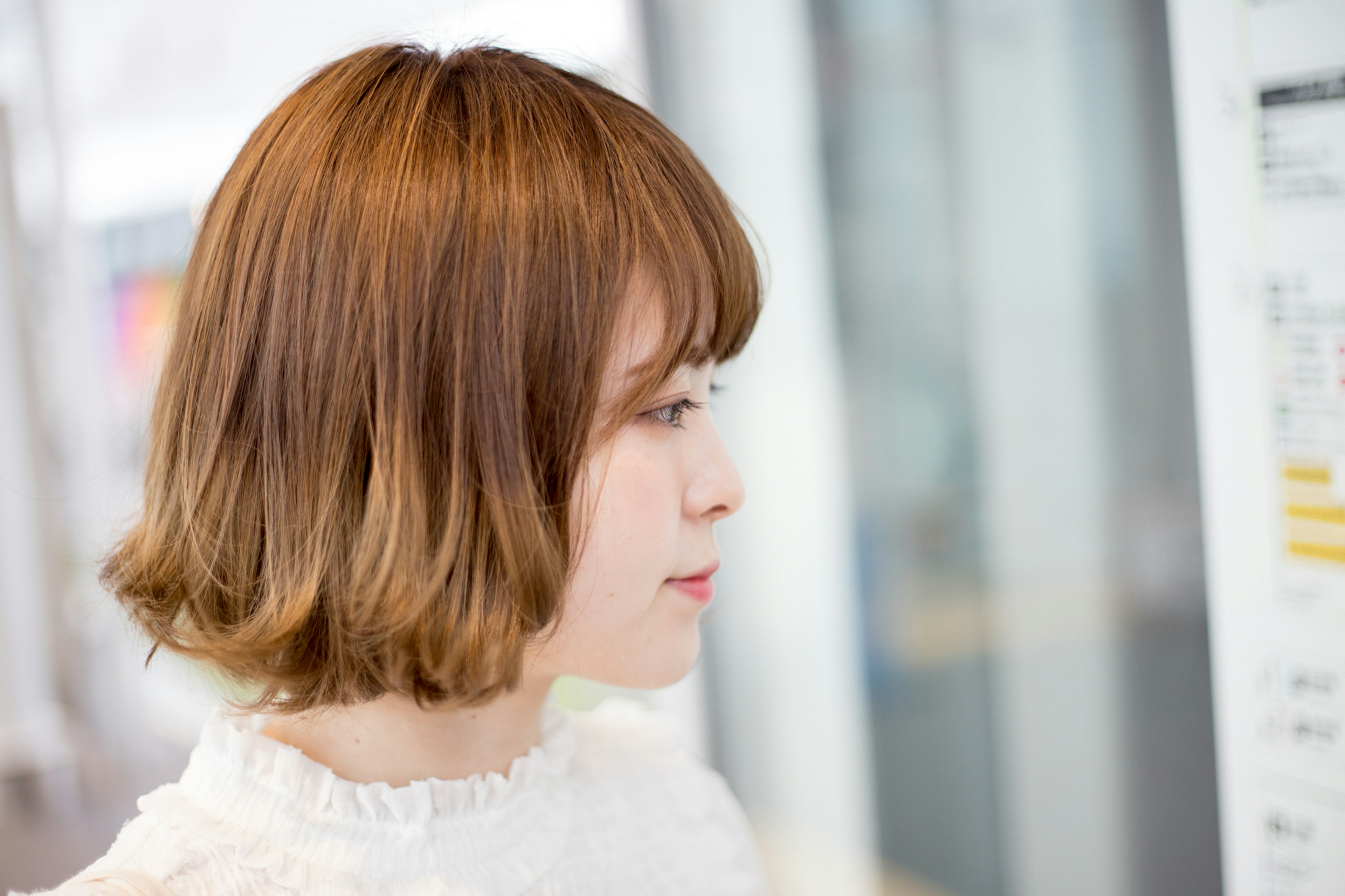 Profile view of a woman with shoulder-length brown hair wearing a white blouse