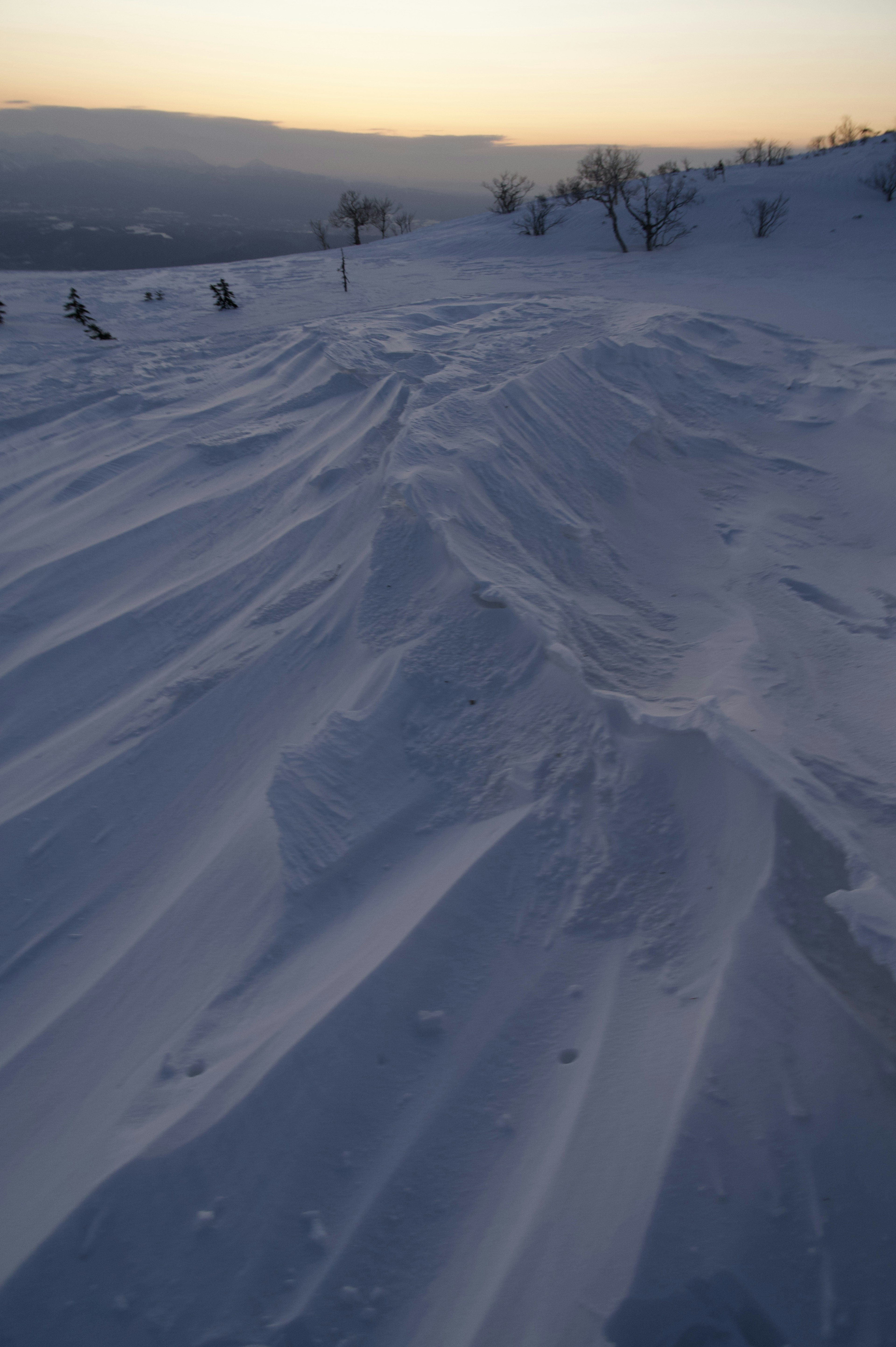 雪の斜面に広がる波紋のような模様と夕暮れの光