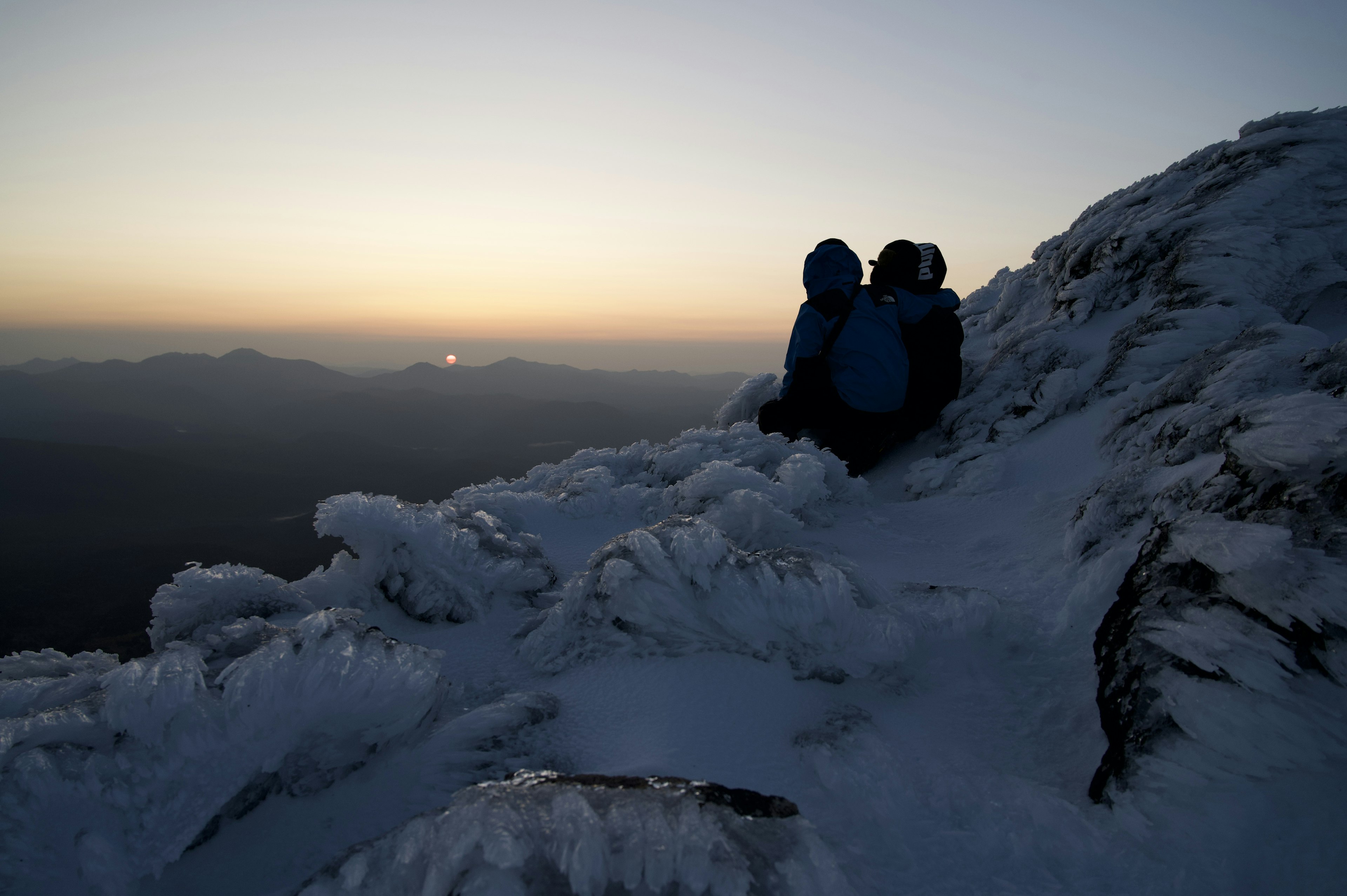 兩名登山者坐在冰冷的岩石上，背景是日落