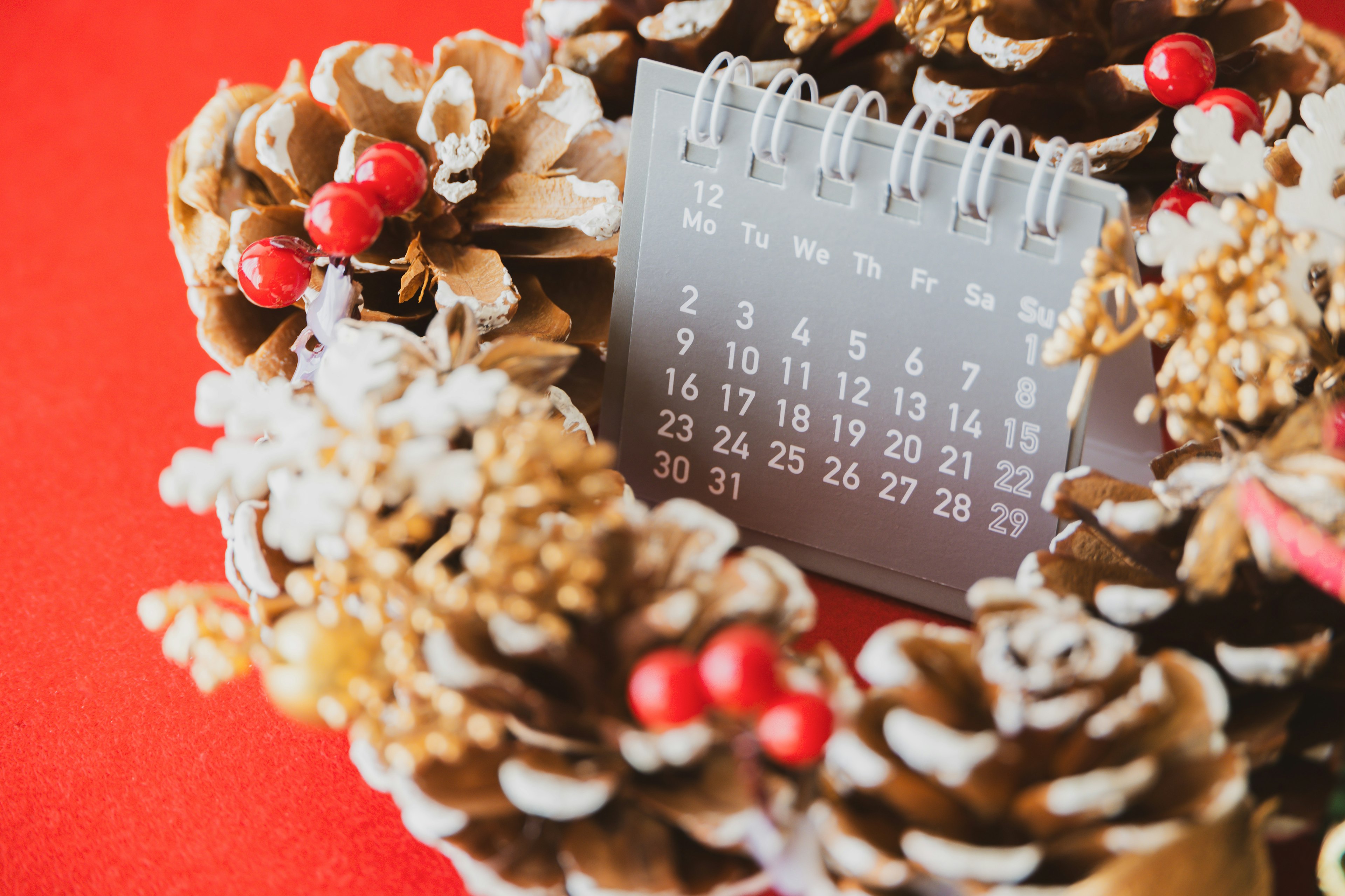 A calendar placed within a Christmas wreath made of pine cones and red berries