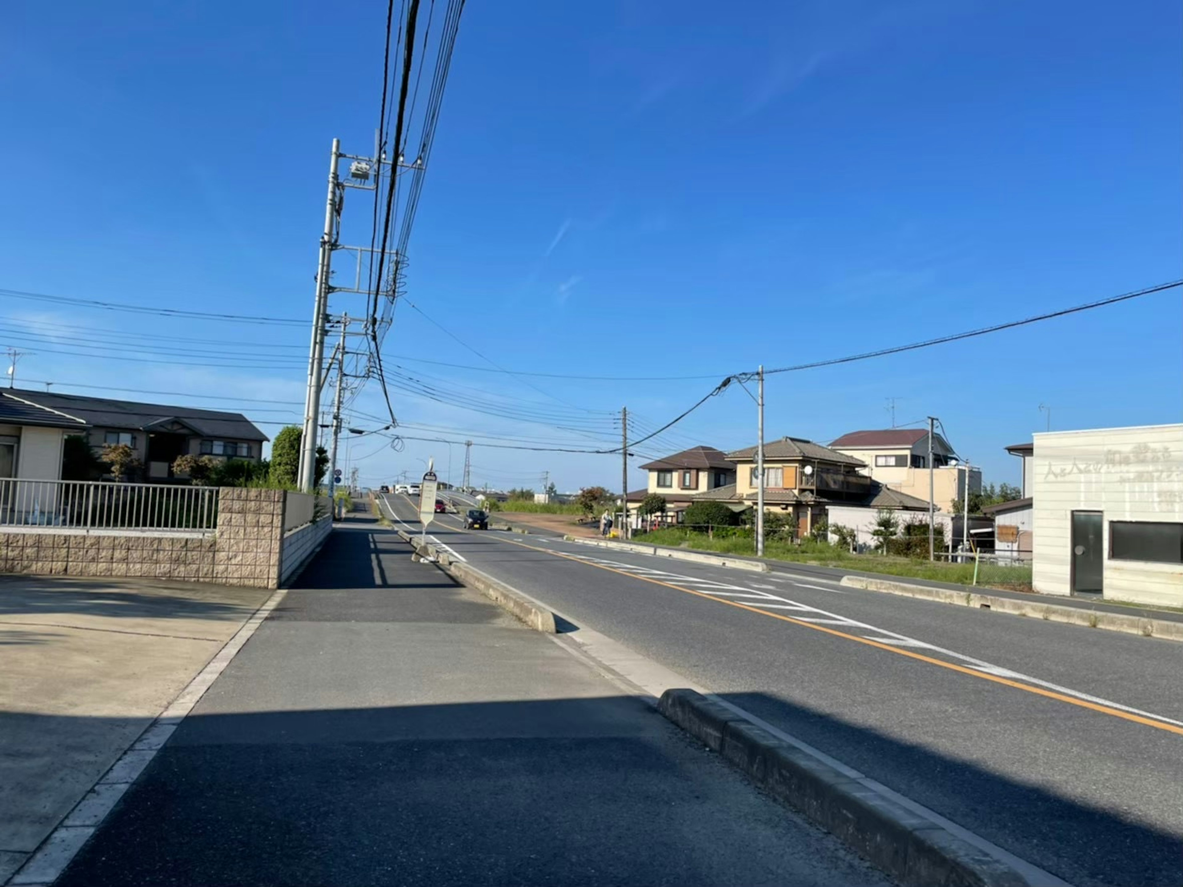 Un quartier résidentiel tranquille sous un ciel bleu avec des lignes électriques et une route