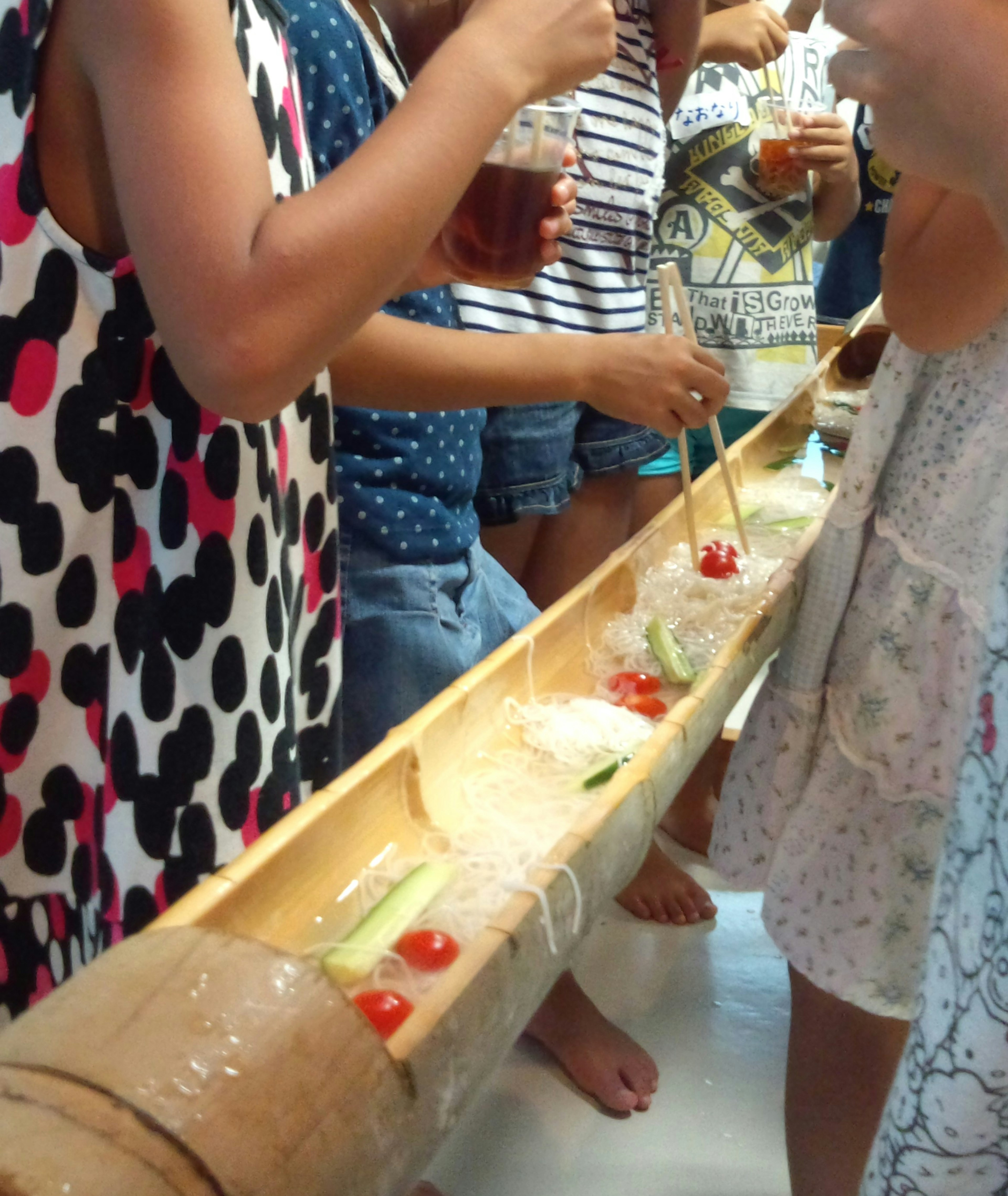 Niños disfrutando de nagashi somen con un tubo de bambú