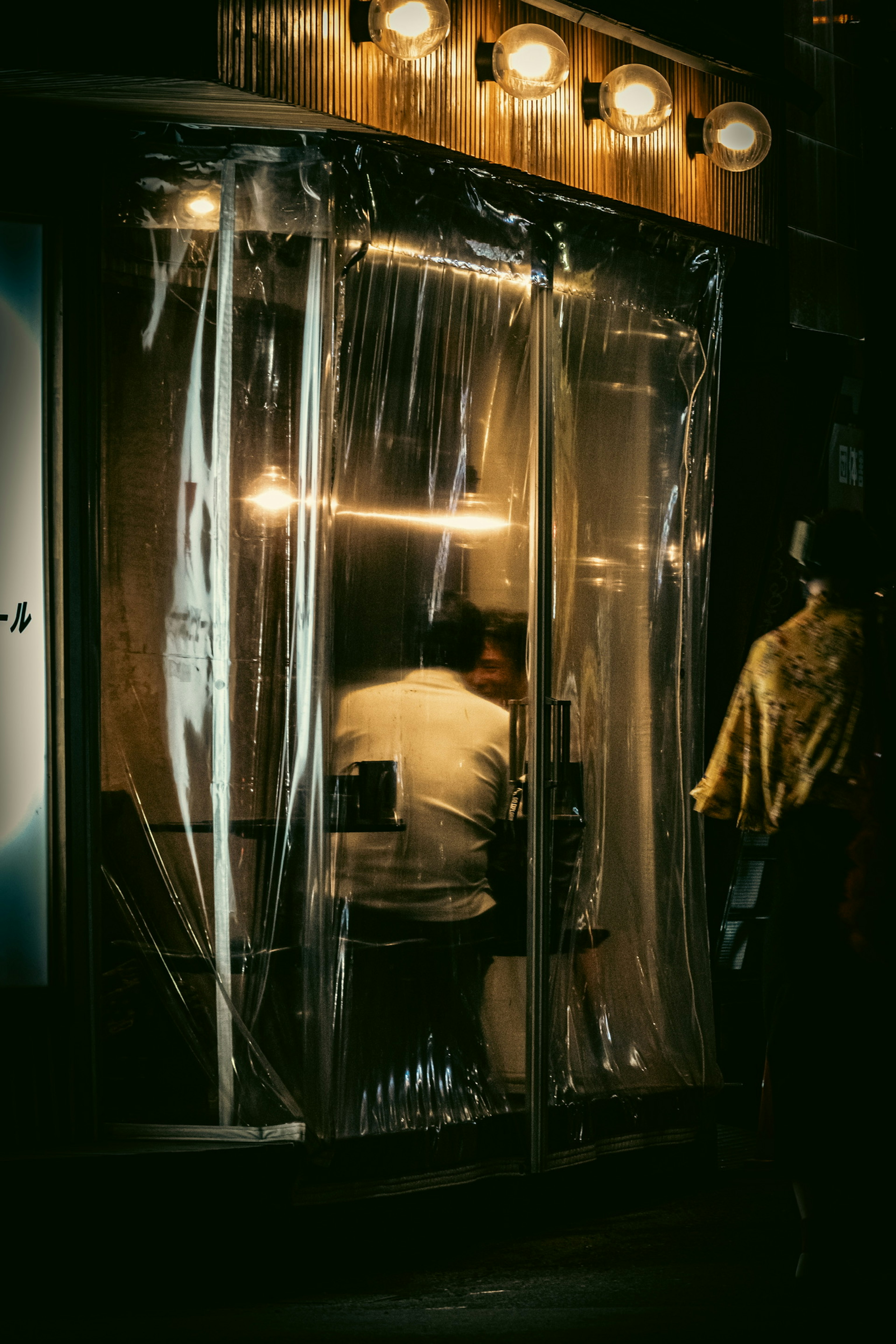 A person seated inside a dimly lit shop covered with plastic sheets