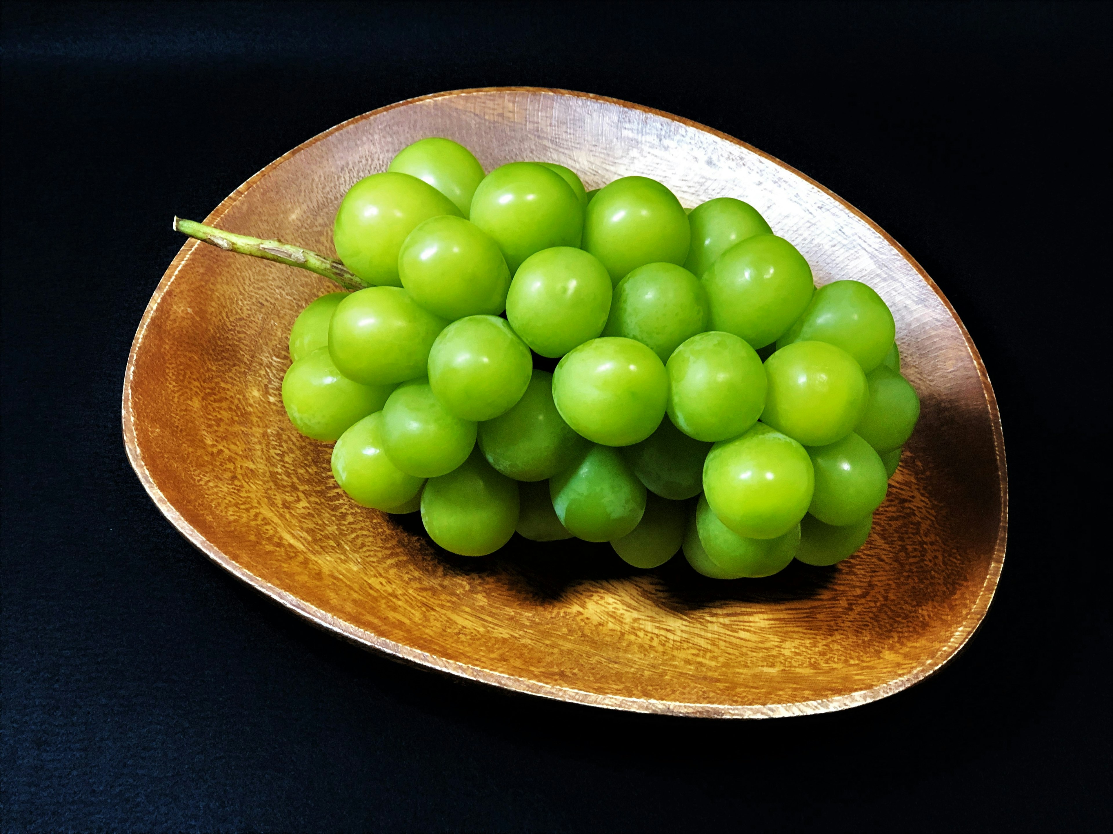 A cluster of fresh green grapes on a wooden plate