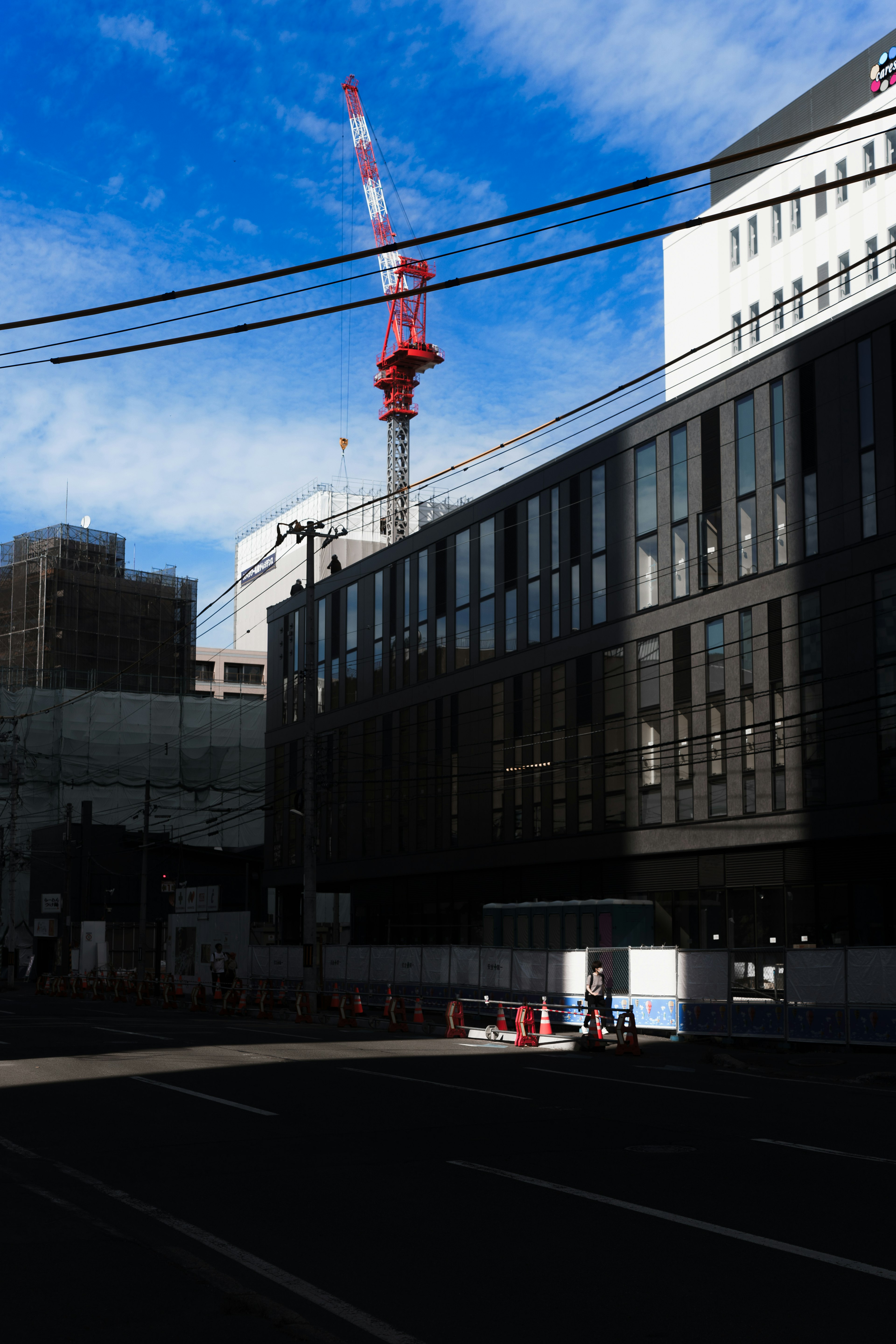 Urban landscape featuring a building and a crane against a blue sky with power lines