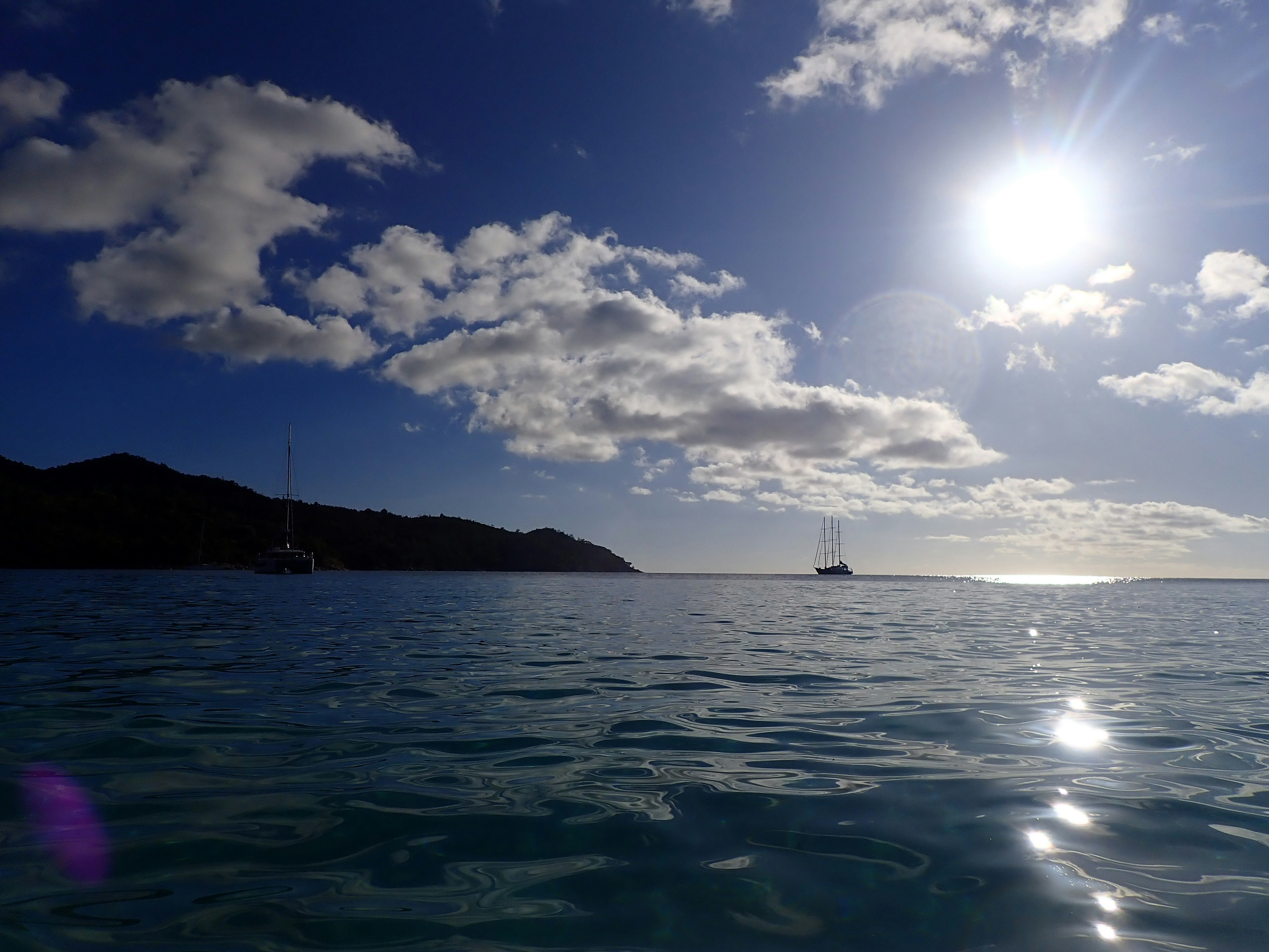 A scenic view of a blue ocean and sky with shining sun and clouds