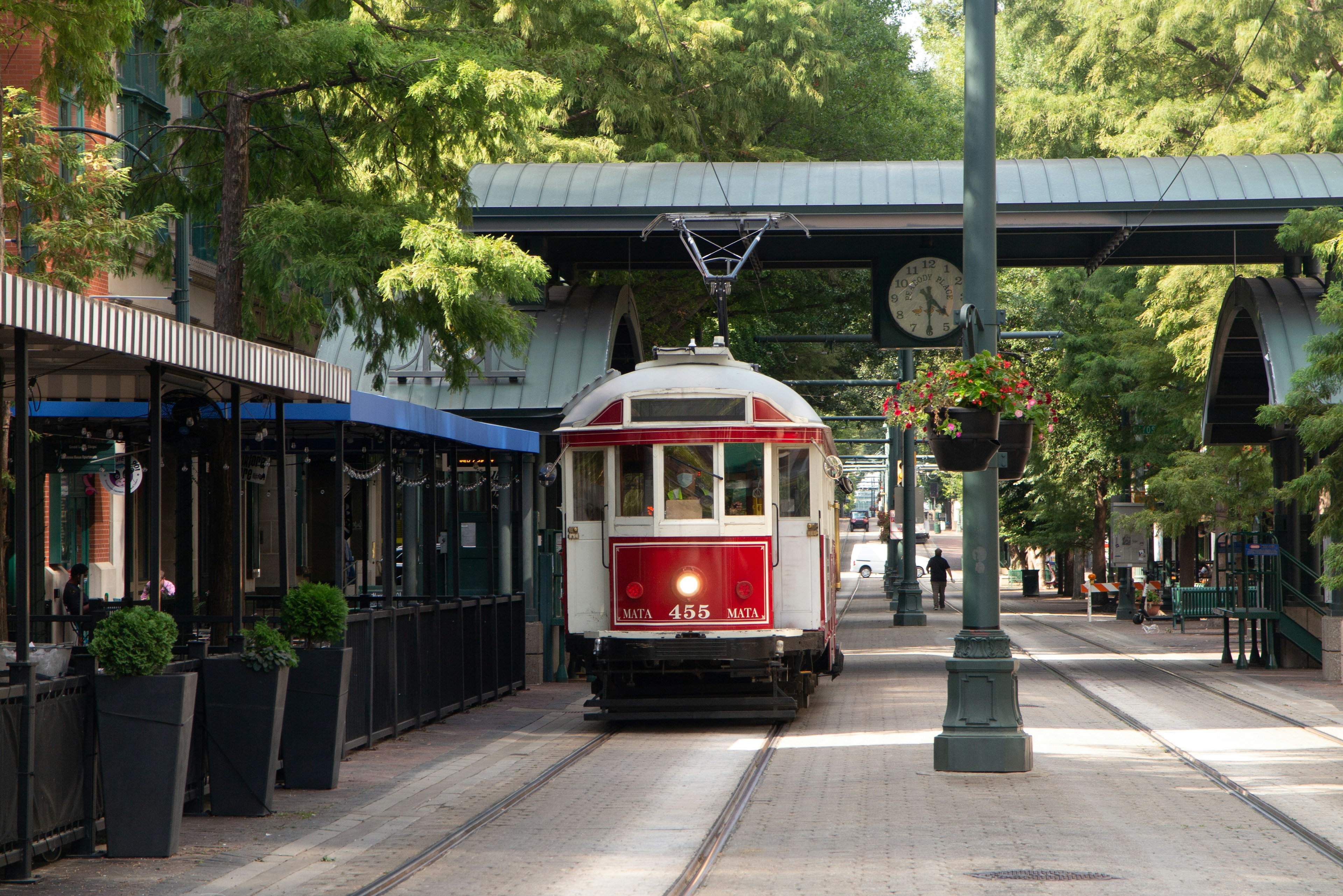 Red and white tram on a street lined with plants and shops