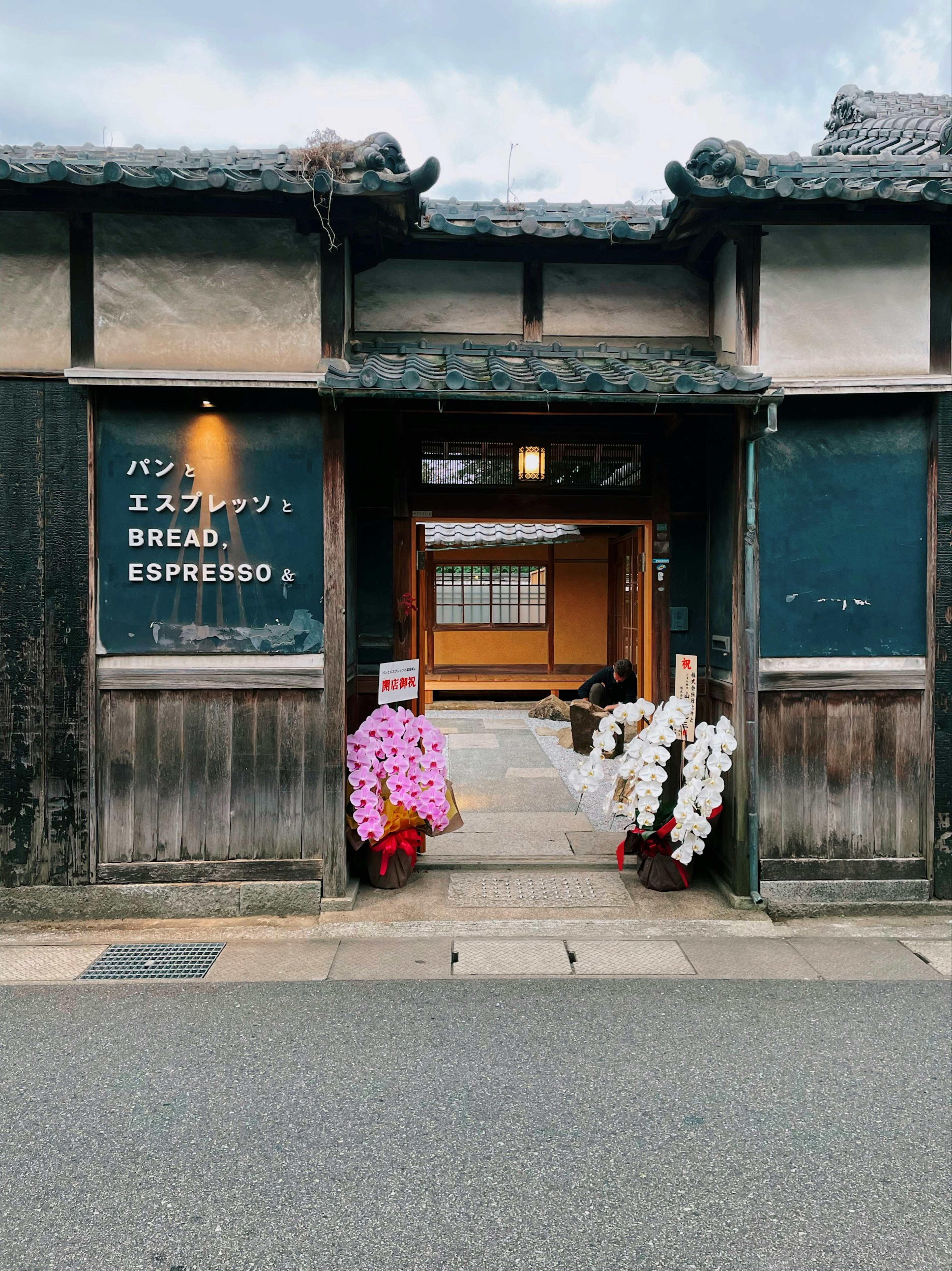 伝統的な日本の建物の入口にあるエスプレッソとパンの看板と色とりどりの花