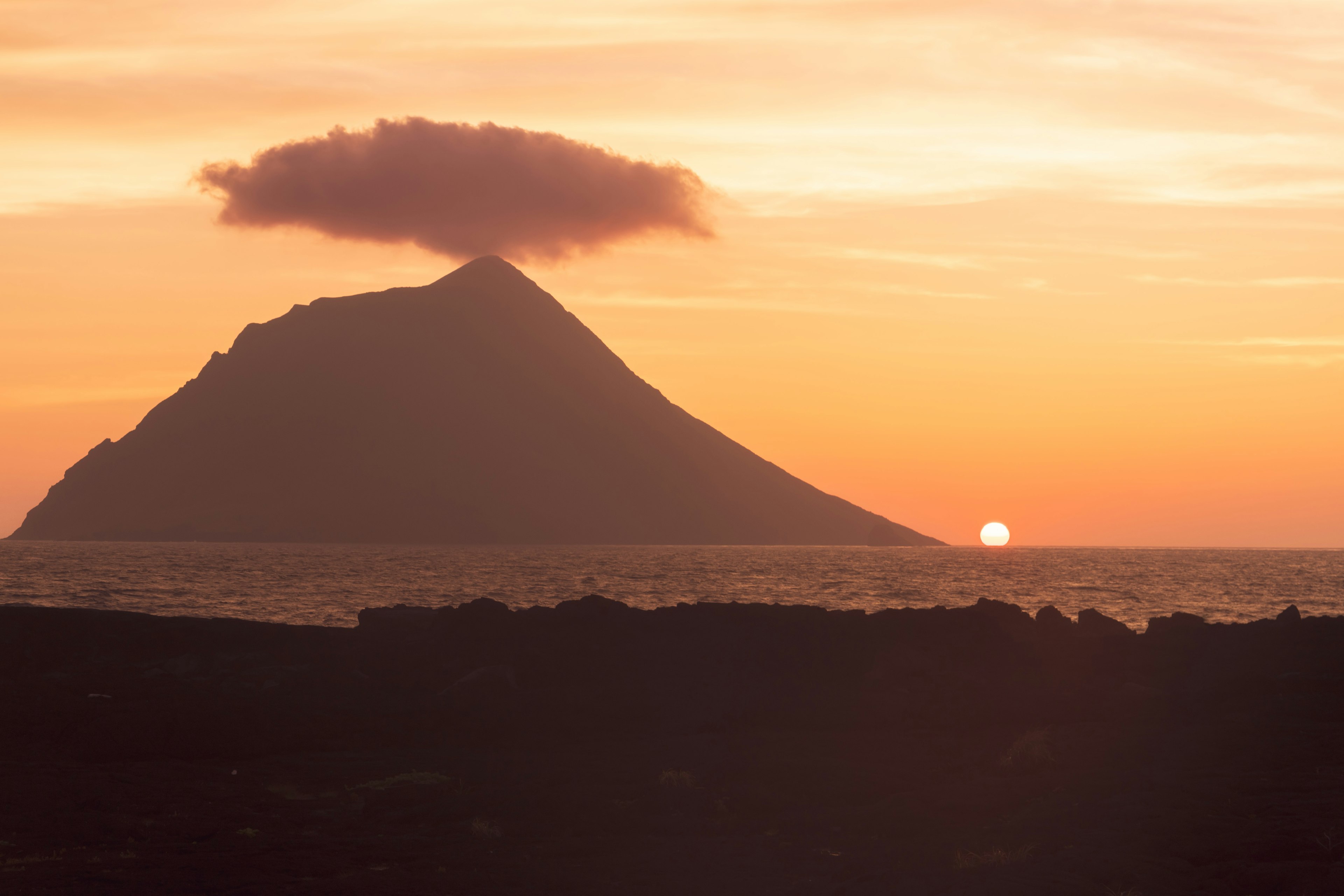 Silhouette of a mountain with a cloud against a sunset